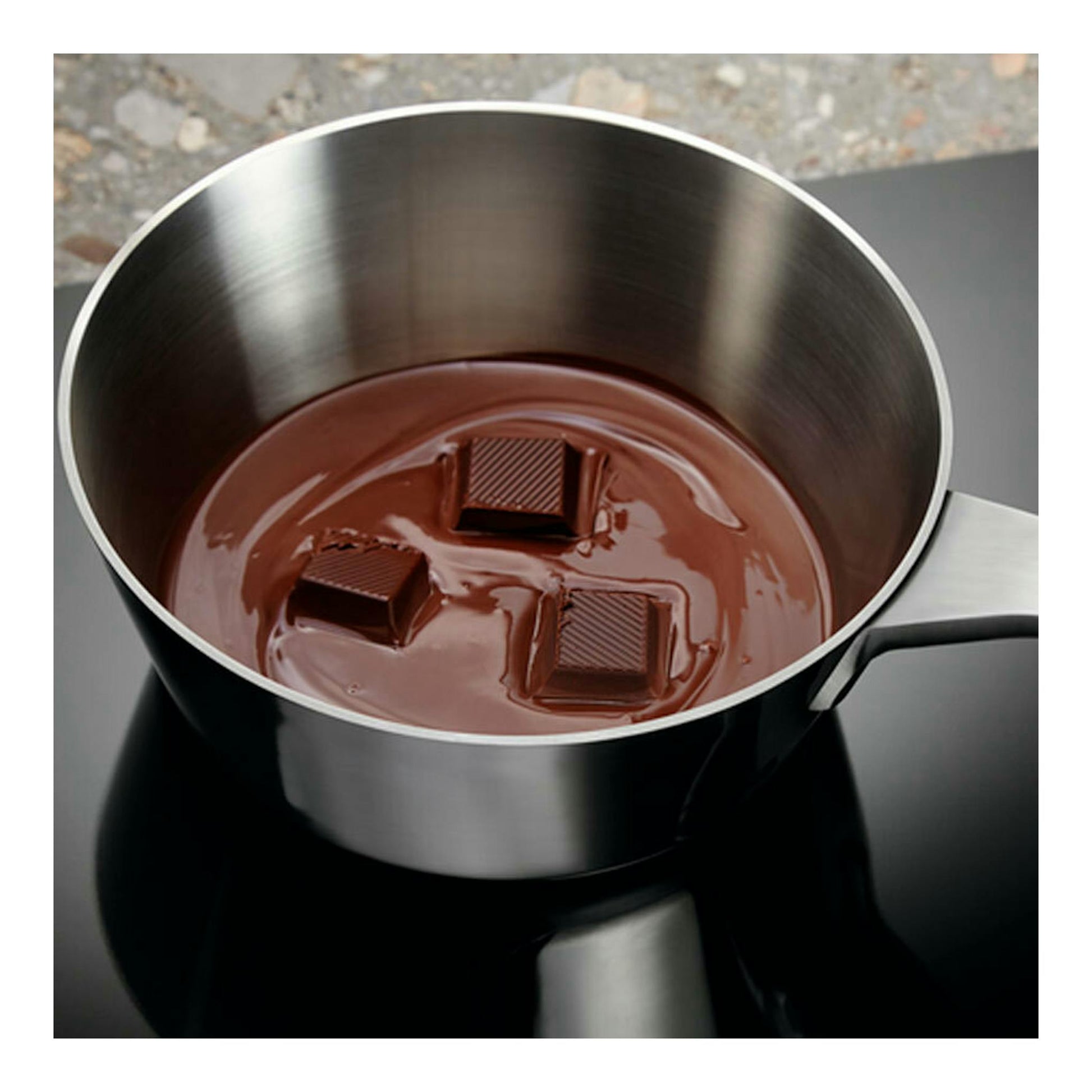 Placa de inducción Electrolux EIV95550 negra, vista superior, con cazo de acero y chocolate fundido.