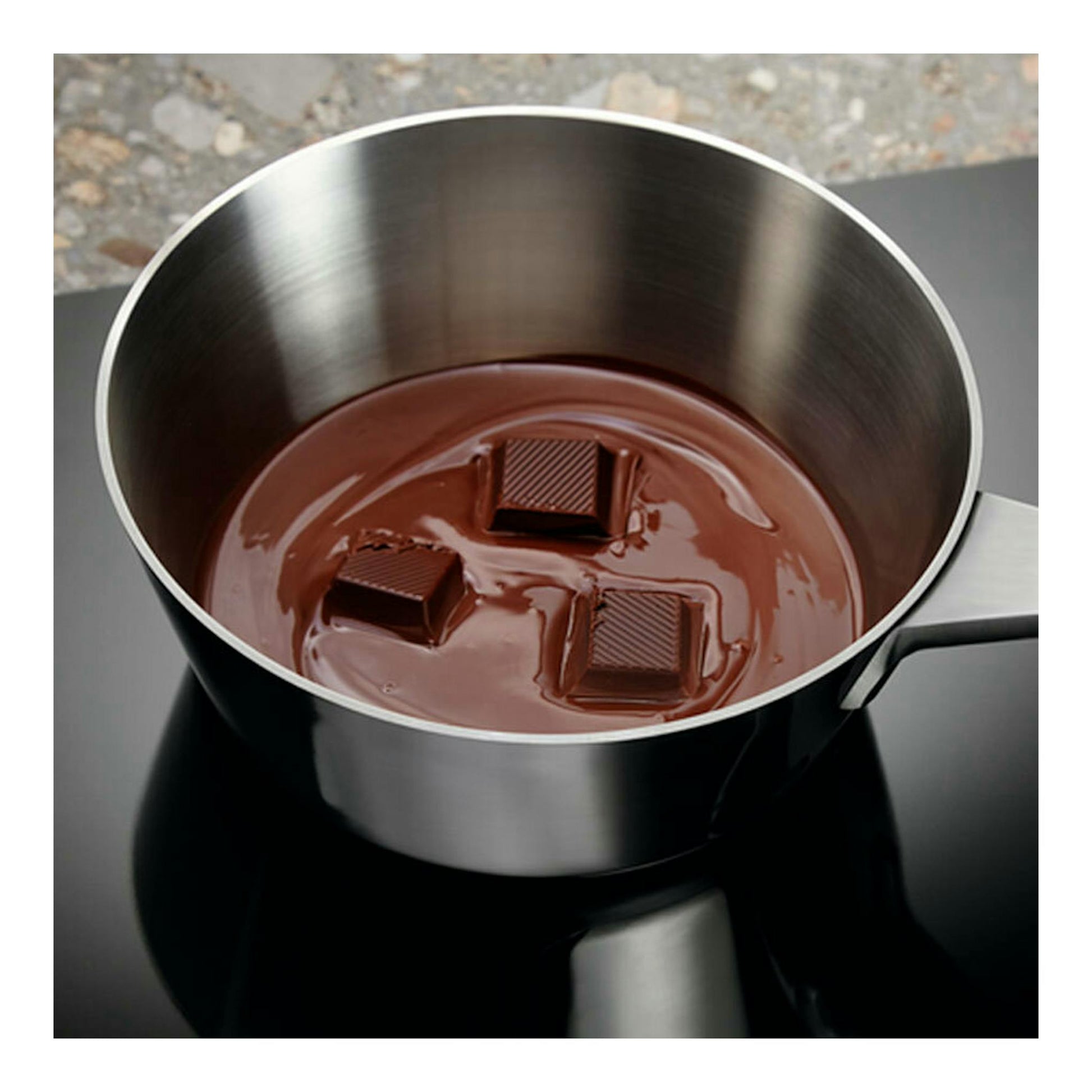 Vista superior de cazo de acero inoxidable sobre placa de inducción negra Electrolux LIT6340CK, con chocolate fundido.