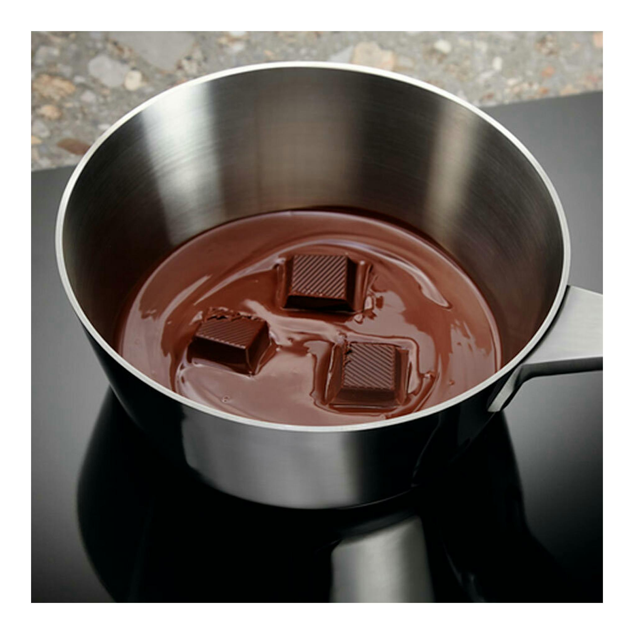 Vista superior de cazo de acero inoxidable sobre placa de inducción negra Electrolux LIT6340CK, con chocolate fundido.