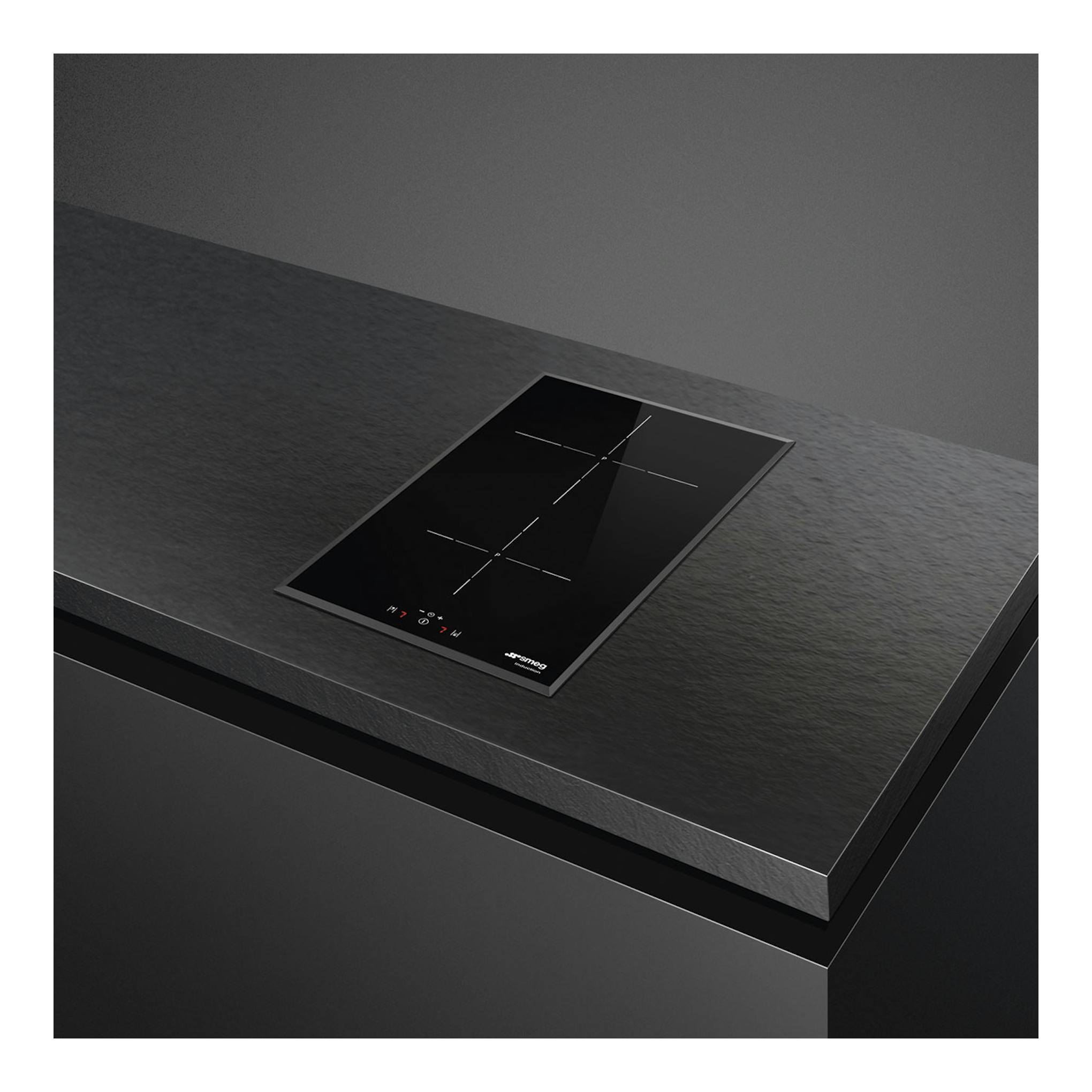 Placa de inducción Smeg SI5322B negra, vista en ángulo sobre encimera oscura, con 2 zonas táctiles.