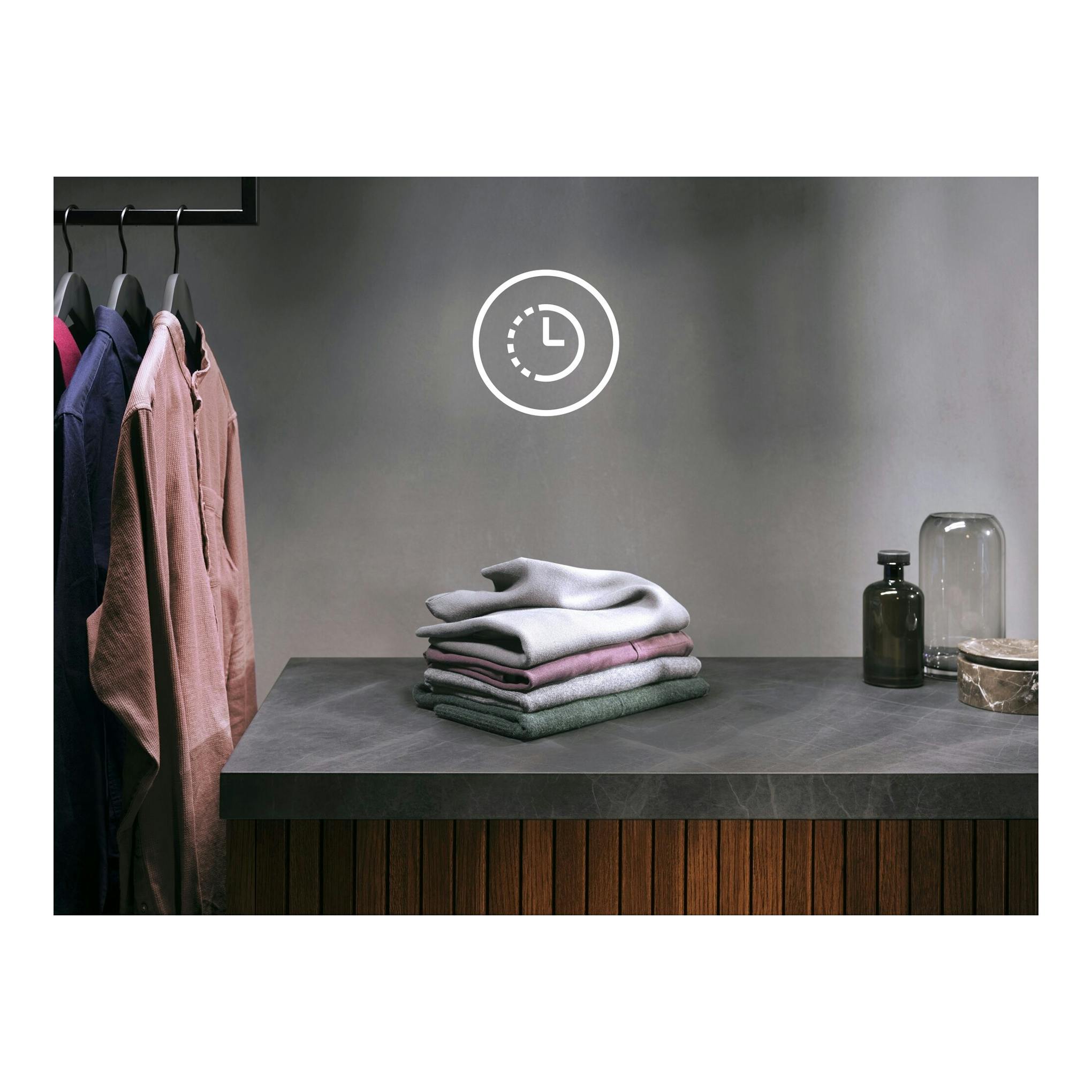 AEG LFE6G54H2B: ropa doblada y colgada en una estancia gris, con icono de reloj en la pared.