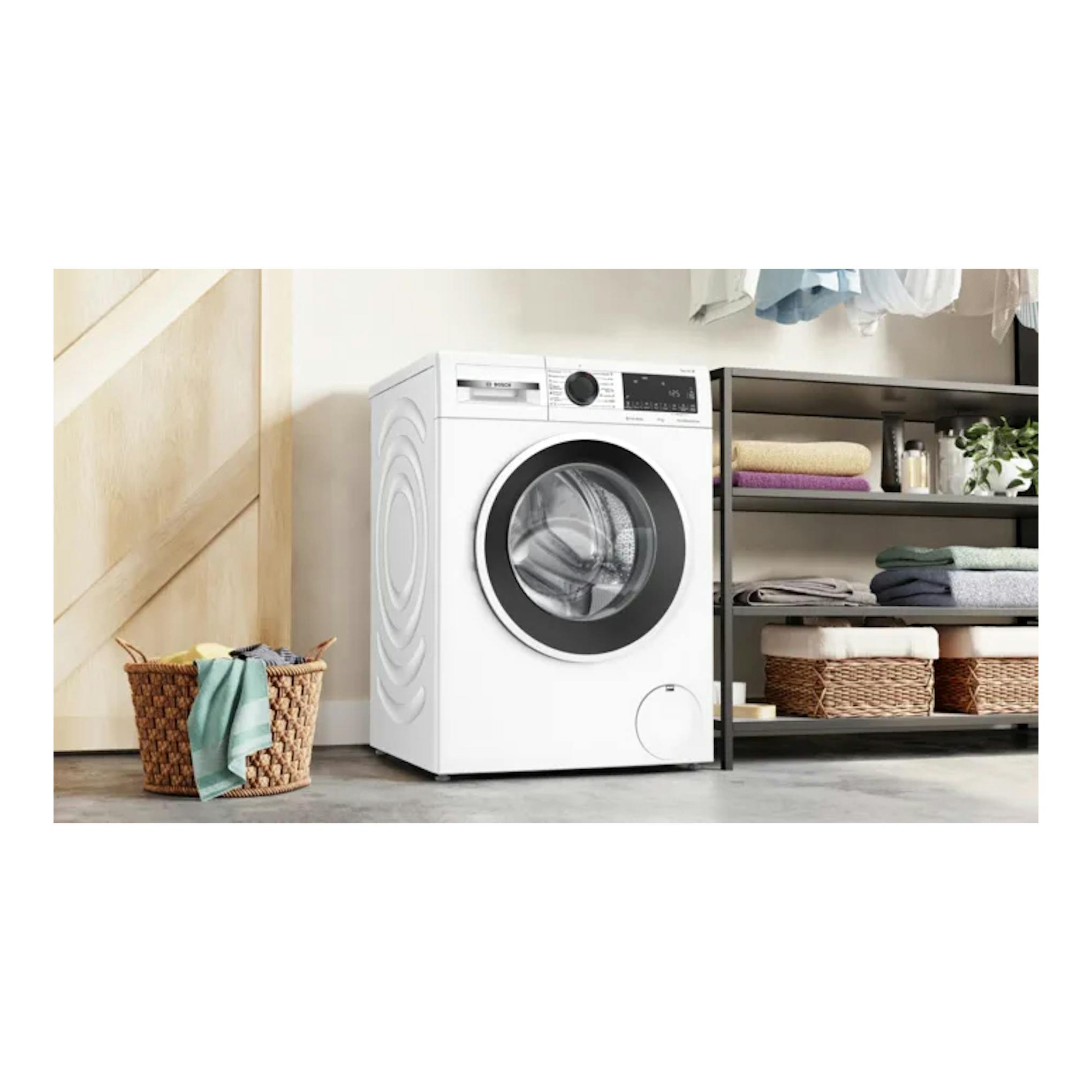 Lavadora Bosch WGG254ZBES blanca, vista frontal, junto a una estantería y una cesta de ropa.