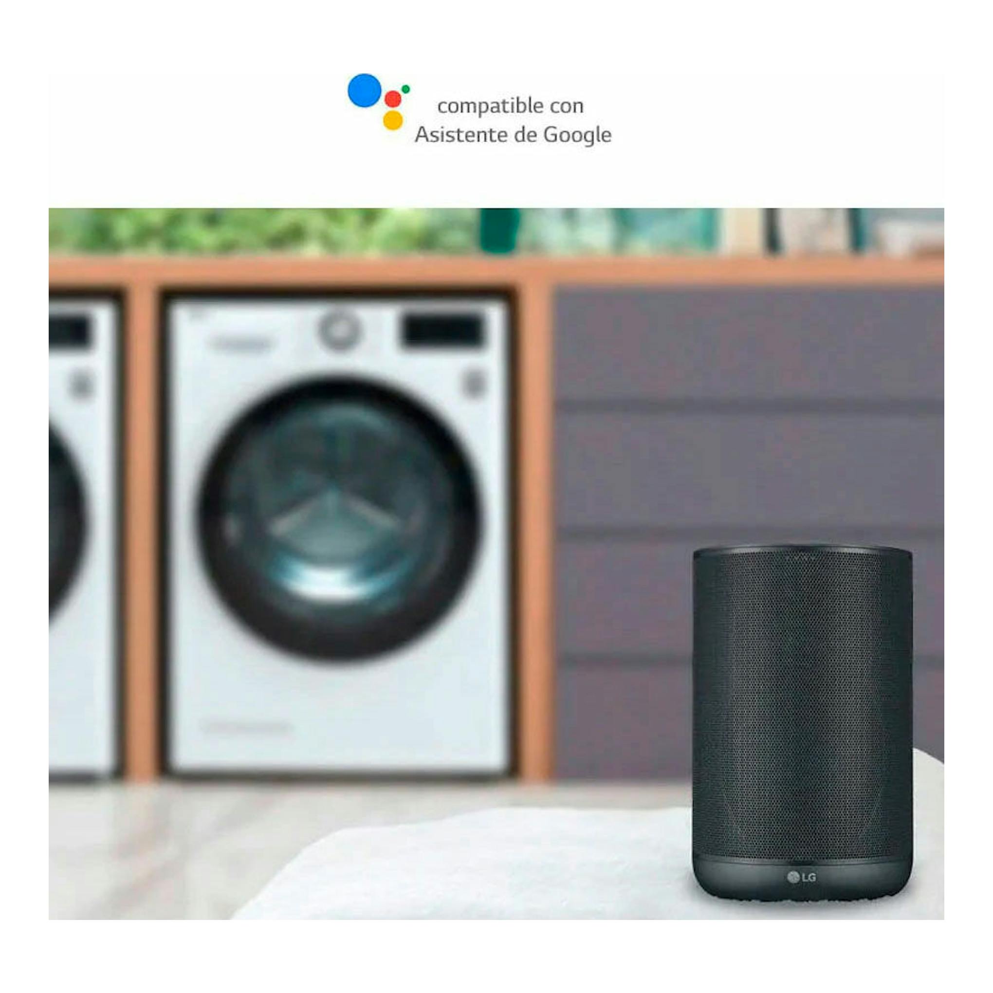 Altavoz inteligente LG negro, vista frontal, con lavadoras desenfocadas al fondo y texto de compatibilidad con Google.