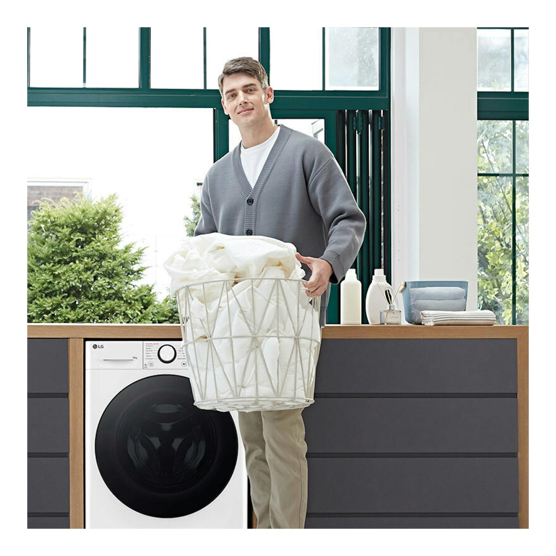 Lavadora LG F4WR6010AGW blanca, carga frontal, con puerta negra; un hombre sostiene una cesta de ropa delante.
