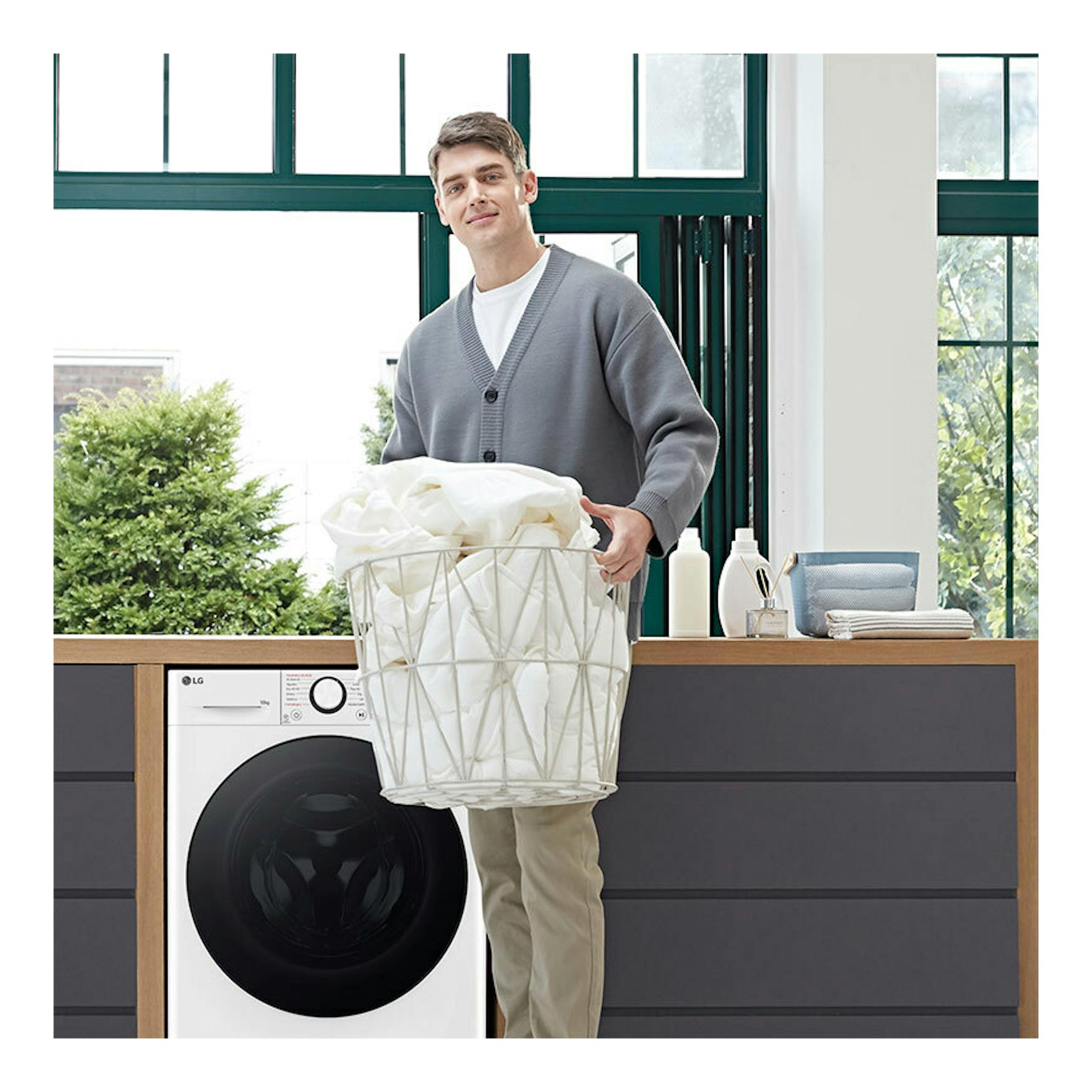 Lavadora LG F4WR6010AGW blanca, carga frontal, con puerta negra; un hombre sostiene una cesta de ropa delante.