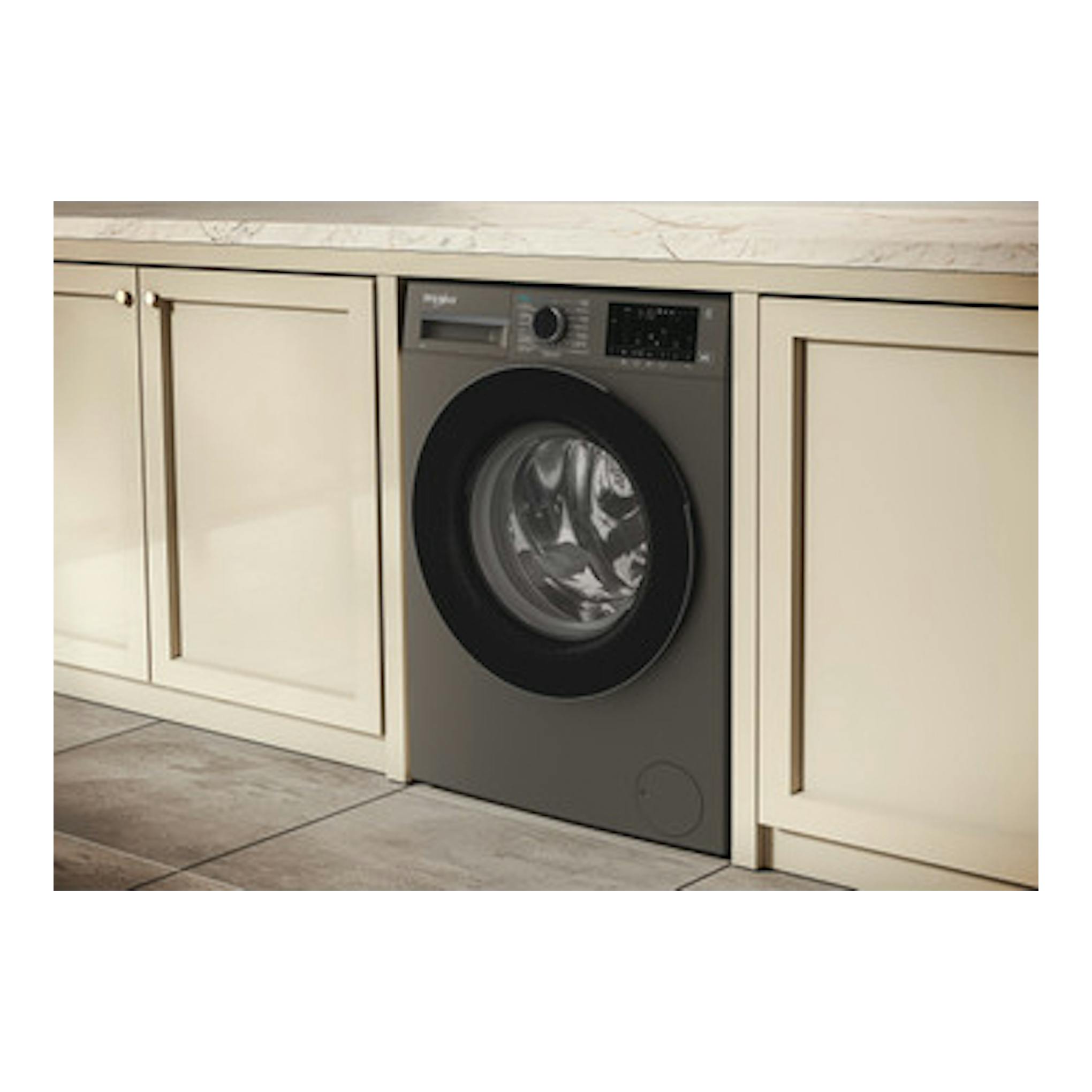 Lavadora Whirlpool WAM 07GB SPT gris, vista frontal empotrada entre muebles de cocina.