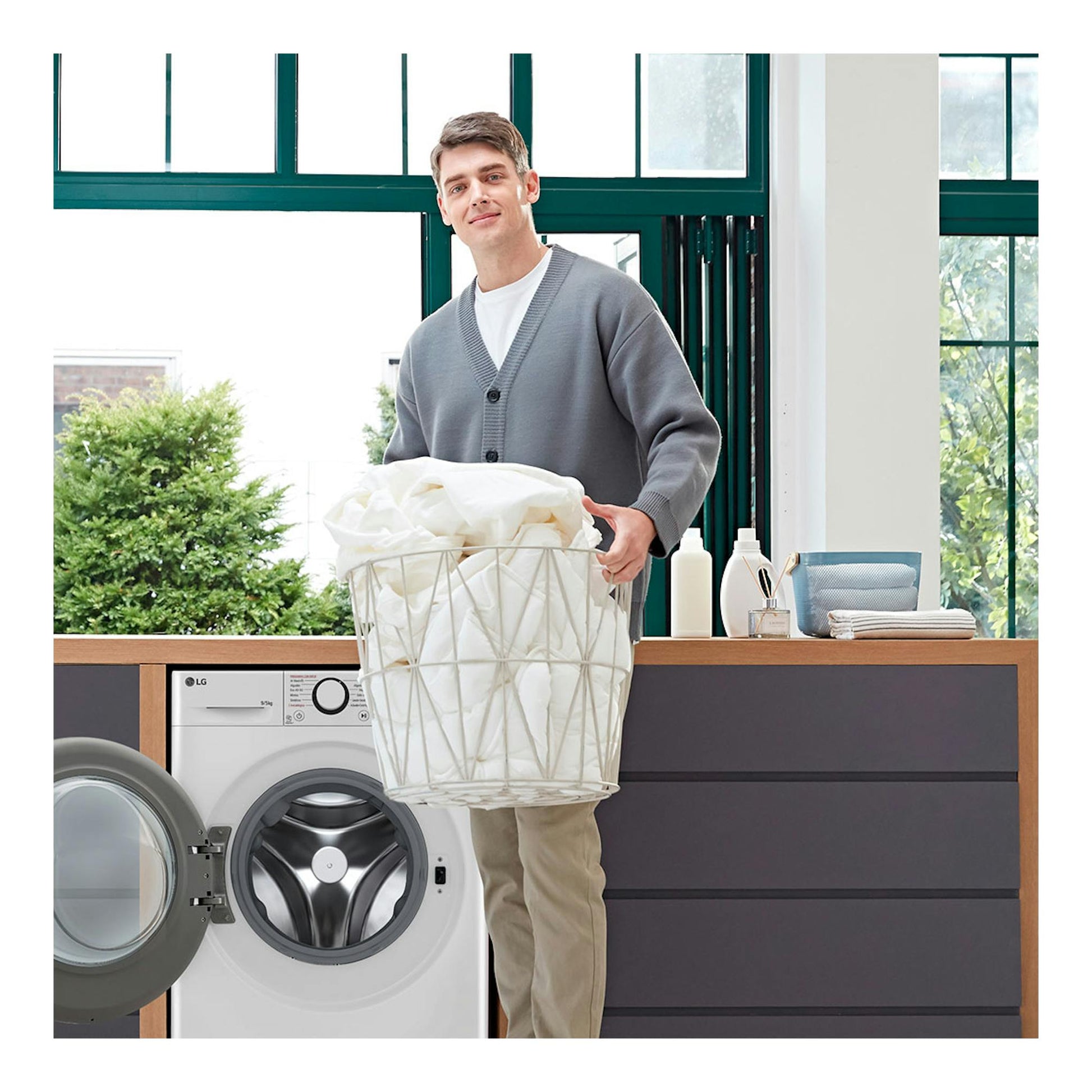 Lavasecadora LG F2DR5S09A1W blanca, vista frontal, con puerta abierta y un hombre con un cesto de ropa.