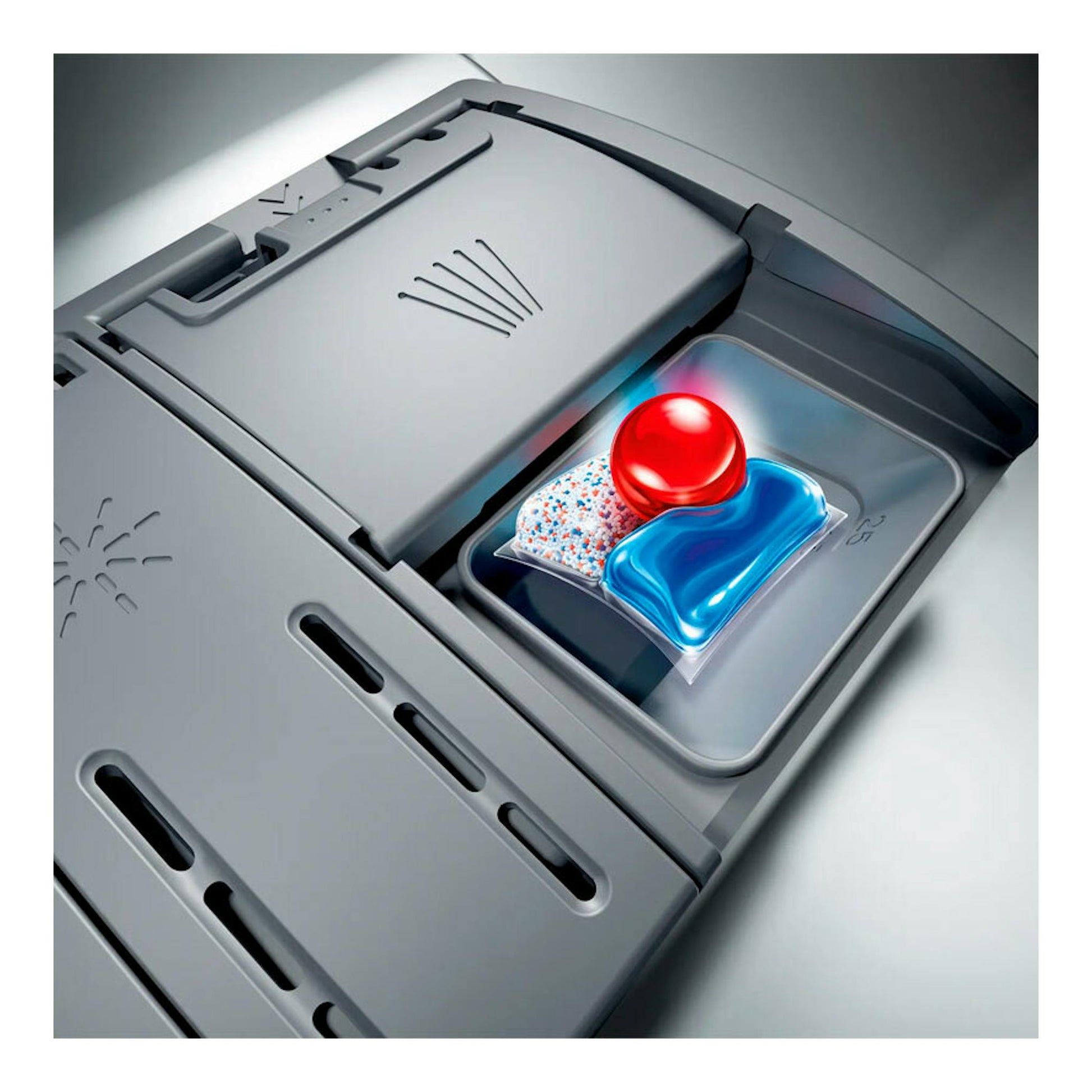 Primer plano de un lavavajillas gris con el dispensador abierto y una cápsula detergente azul y roja.