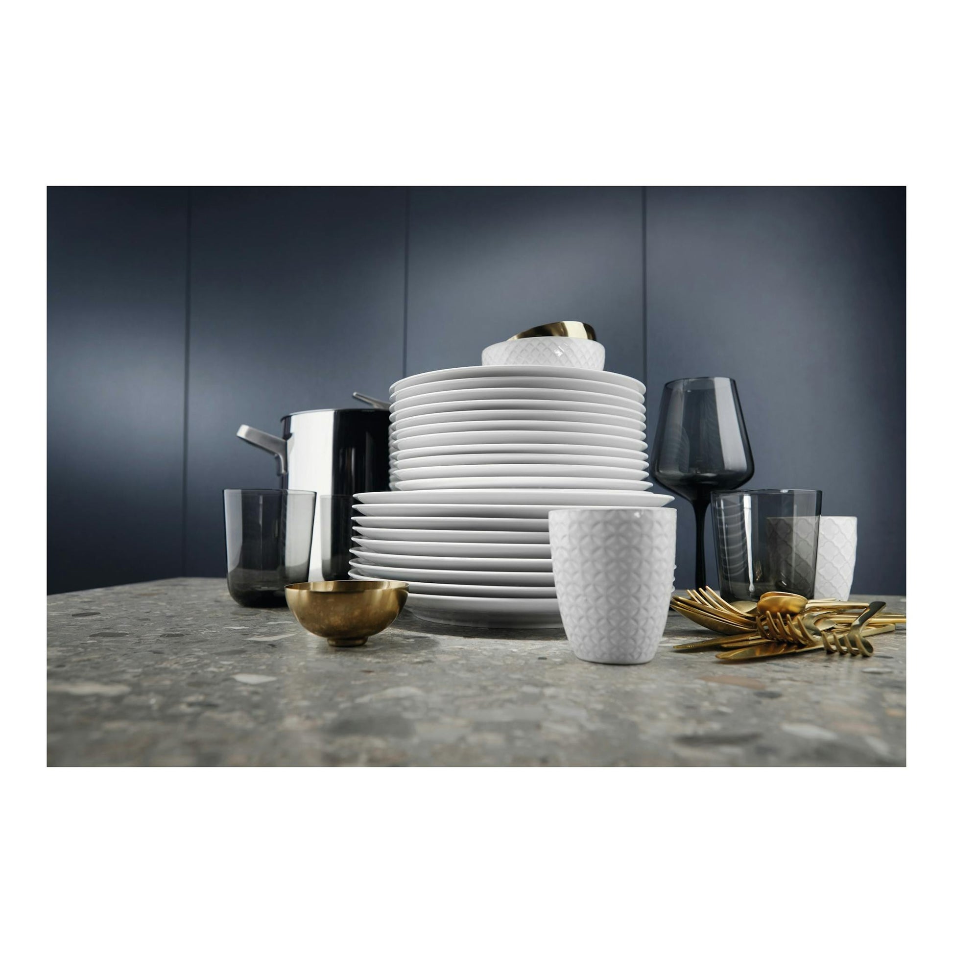 Electrolux EEA27205L: vajilla apilada con platos, vasos y cubiertos dorados sobre encimera gris, vista frontal.