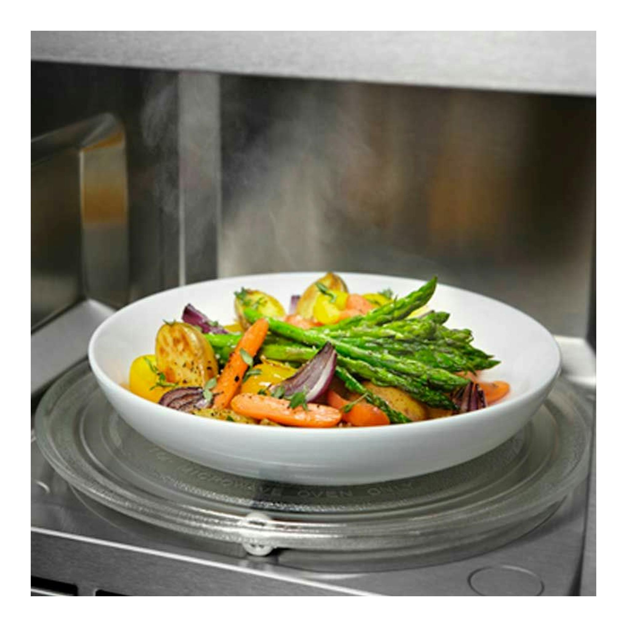 Microondas Electrolux KMFD264TEX, vista interior con plato giratorio y bol blanco con verduras mixtas.