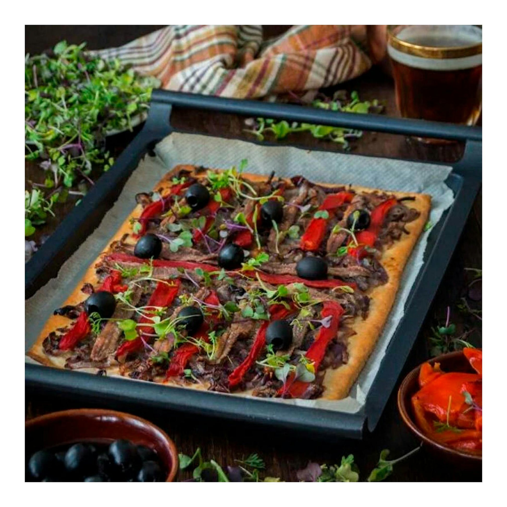Parrilla plana Bra Efficient de 35 cm, negra, vista en ángulo, con una pizza sobre papel de hornear.