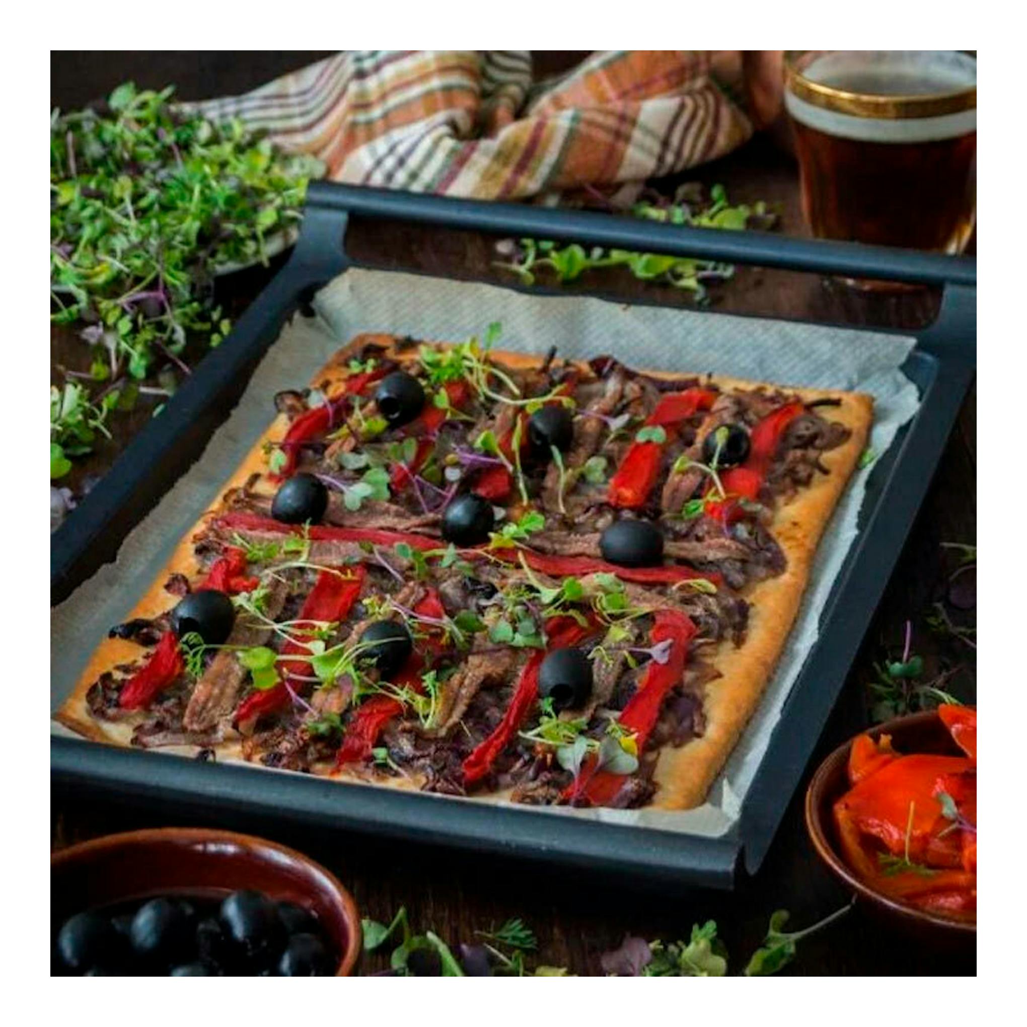 Parrilla plana Bra Efficient de 35 cm, negra, vista en ángulo, con una pizza sobre papel de hornear.