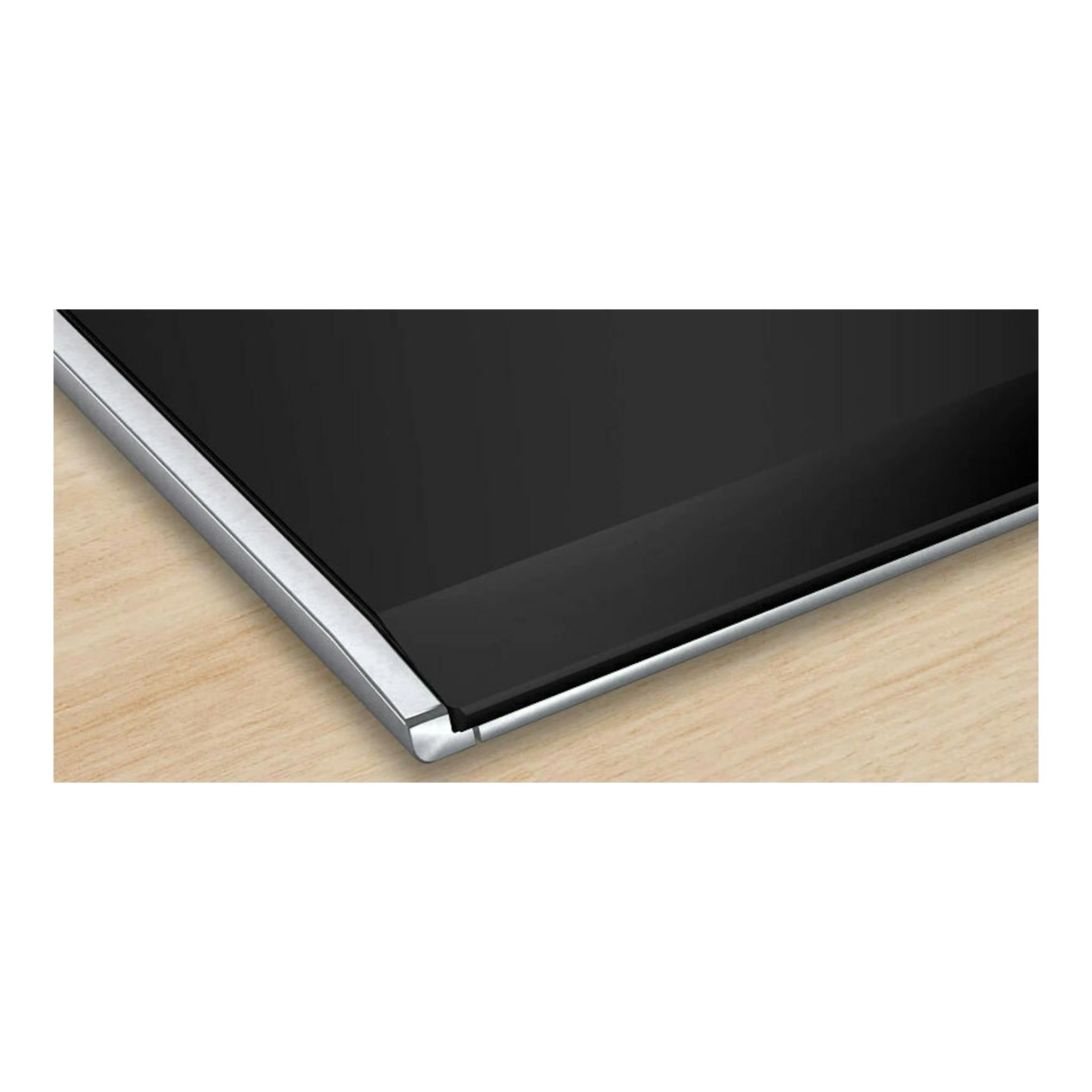 Placa de inducción Bosch PID675HC1E negra, vista en ángulo, con borde metálico sobre encimera de madera.