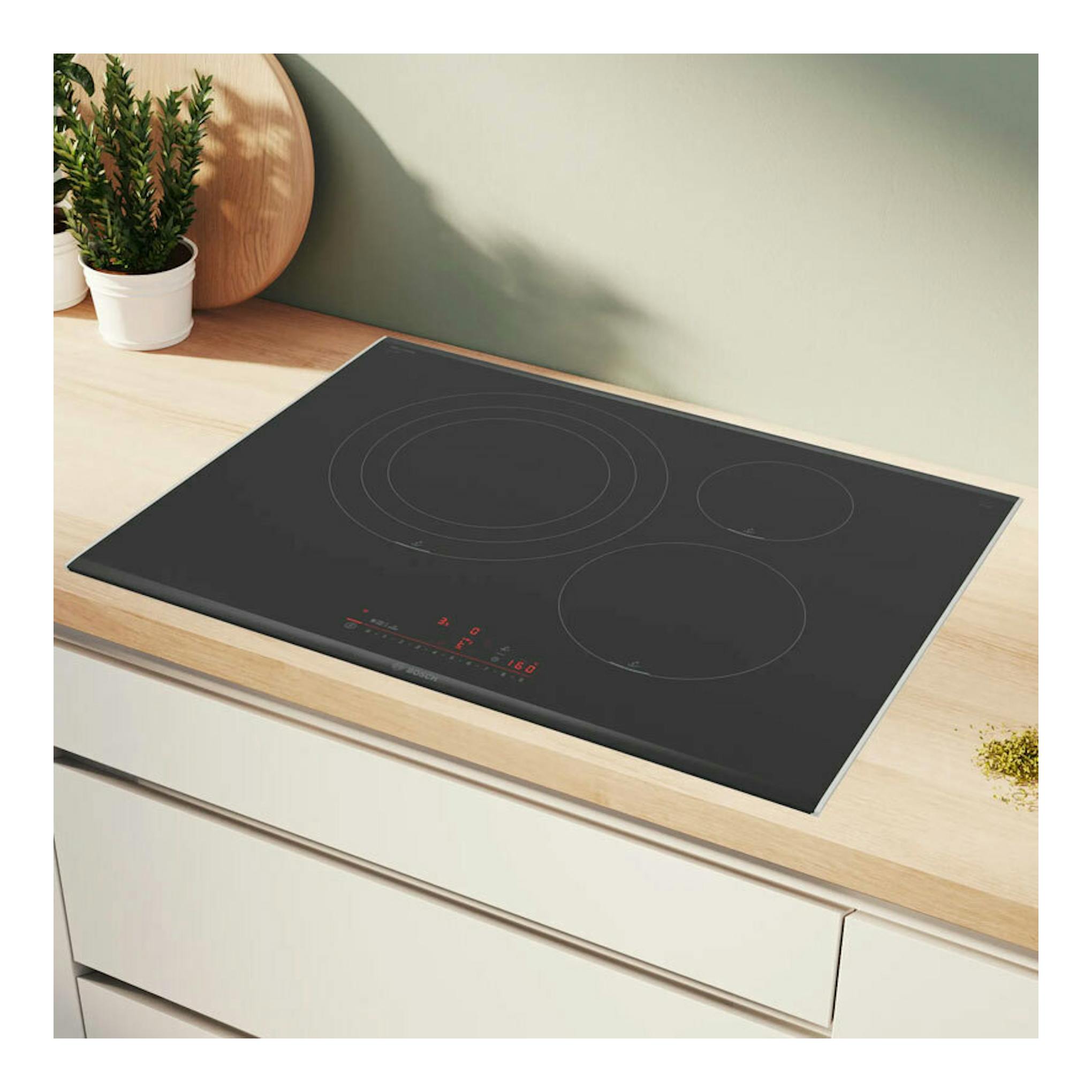 Placa de inducción Bosch PID775HC1E negra, vista superior inclinada sobre encimera de madera.