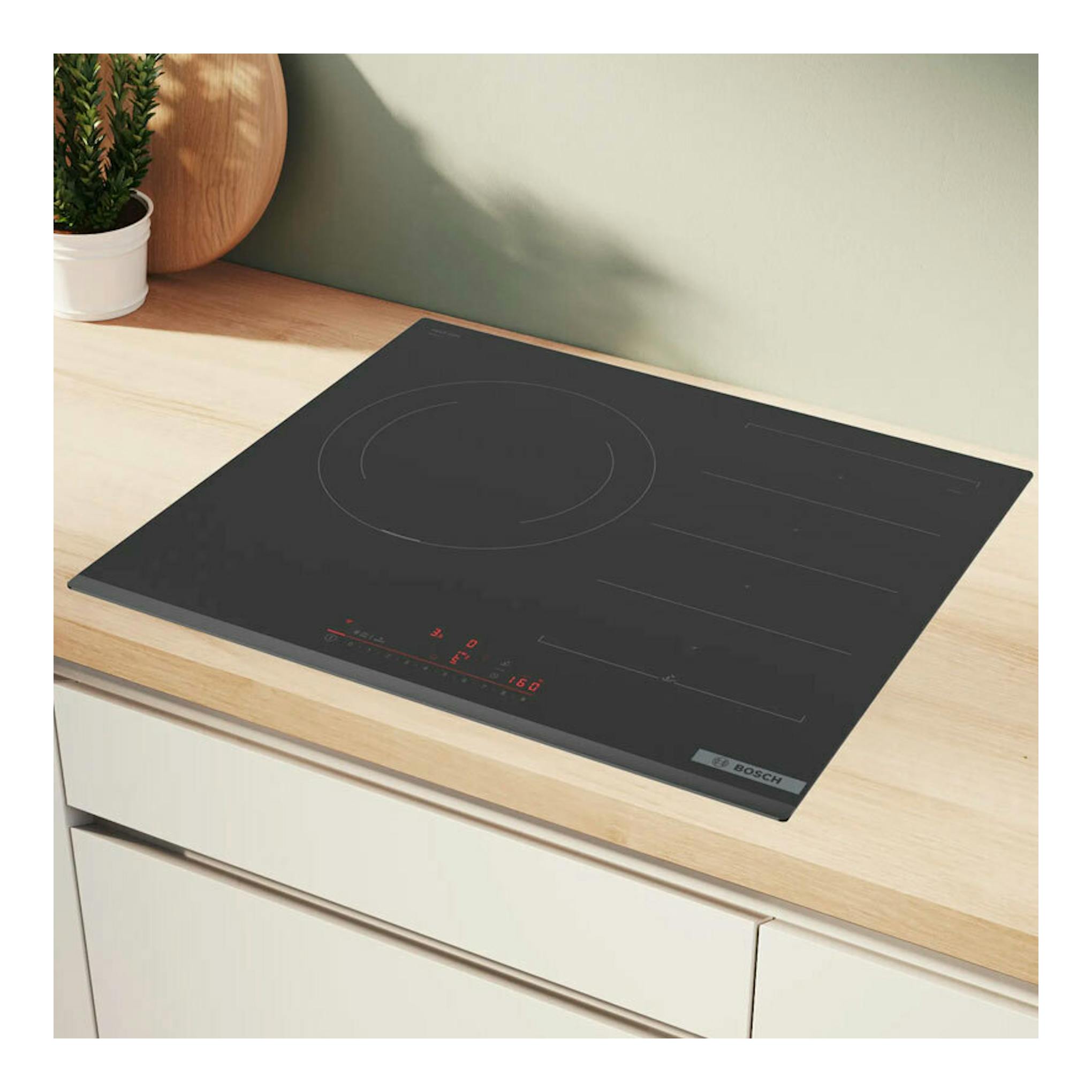 Placa de inducción Bosch PXJ631HC2E negra, vista en ángulo sobre encimera de madera, con controles táctiles rojos.