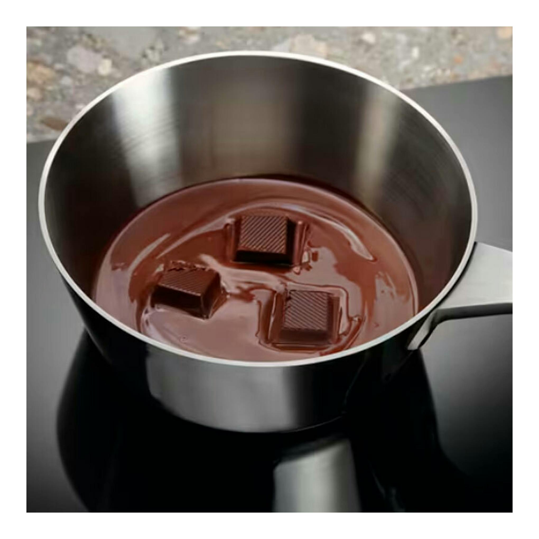 Placa de inducción Electrolux EIT60342, vista superior, con cazo de acero inoxidable y chocolate sobre vidrio negro.