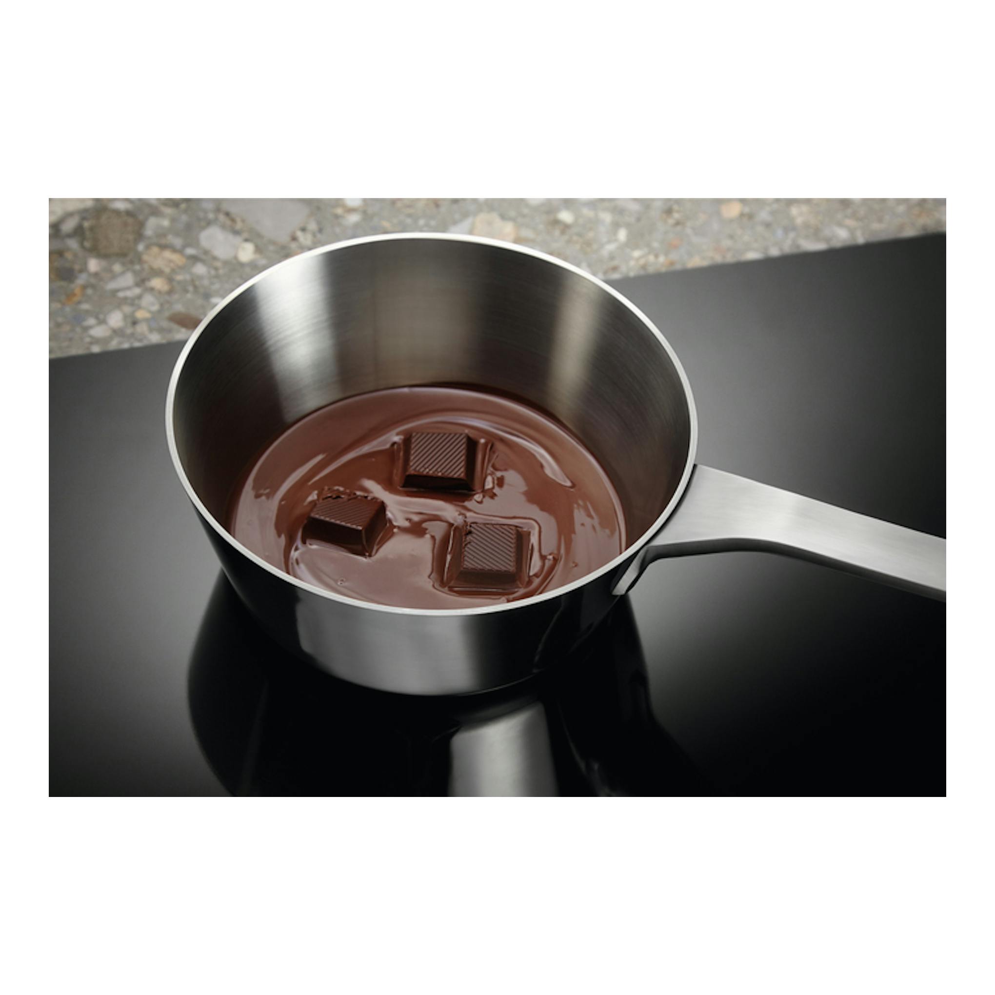 Vista cenital de placa de inducción Electrolux EIT61336CB negra con cazo de chocolate derretido.