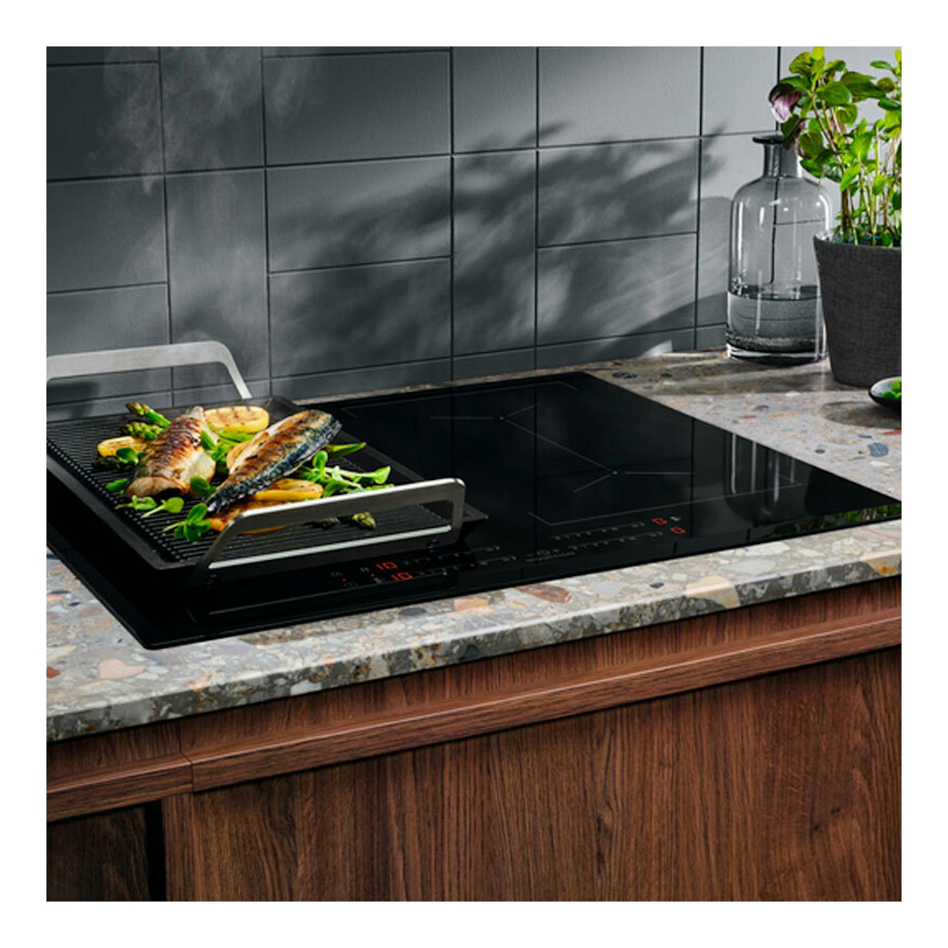Placa de inducción Electrolux EIV644 negra, vista frontal, con bandeja grill y pescado en encimera.