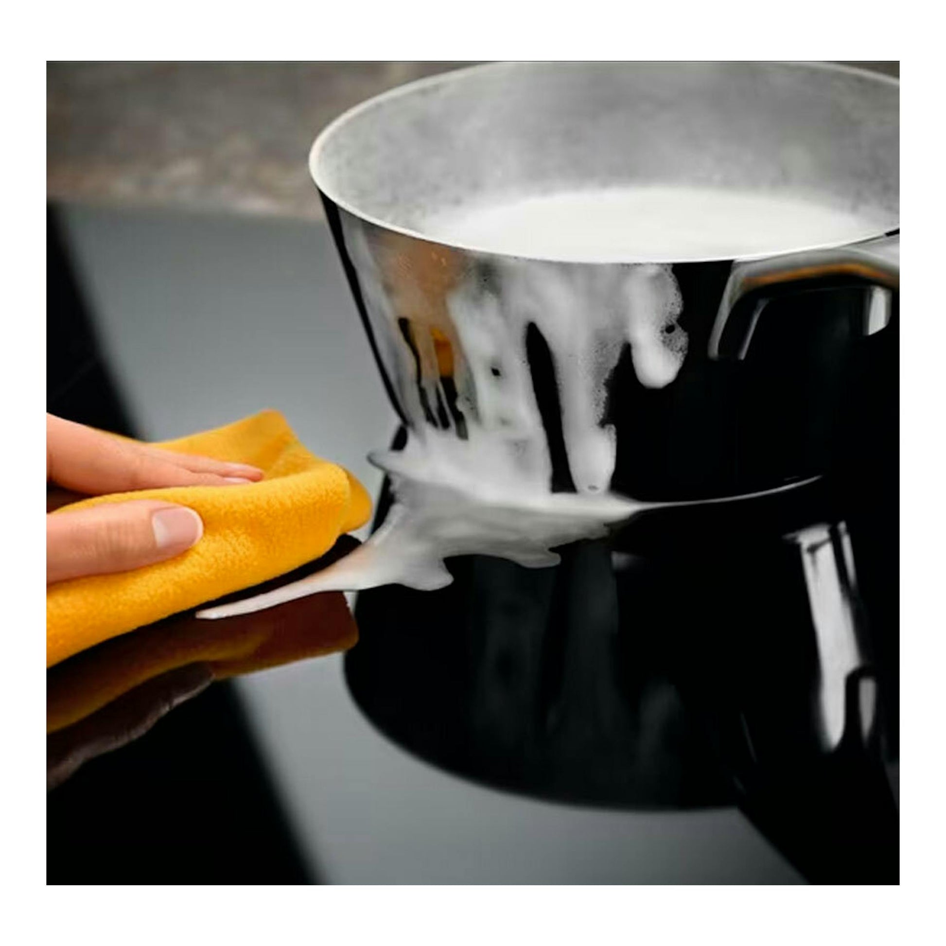 Placa de inducción Electrolux EIV644 negra, con una olla derramada y una mano limpiando con paño amarillo.