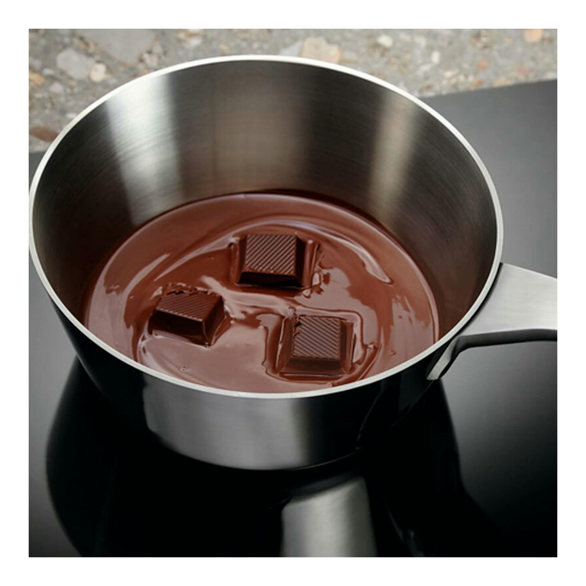 Placa de inducción Electrolux EIV644, cazo de acero con chocolate fundido sobre placa negra.