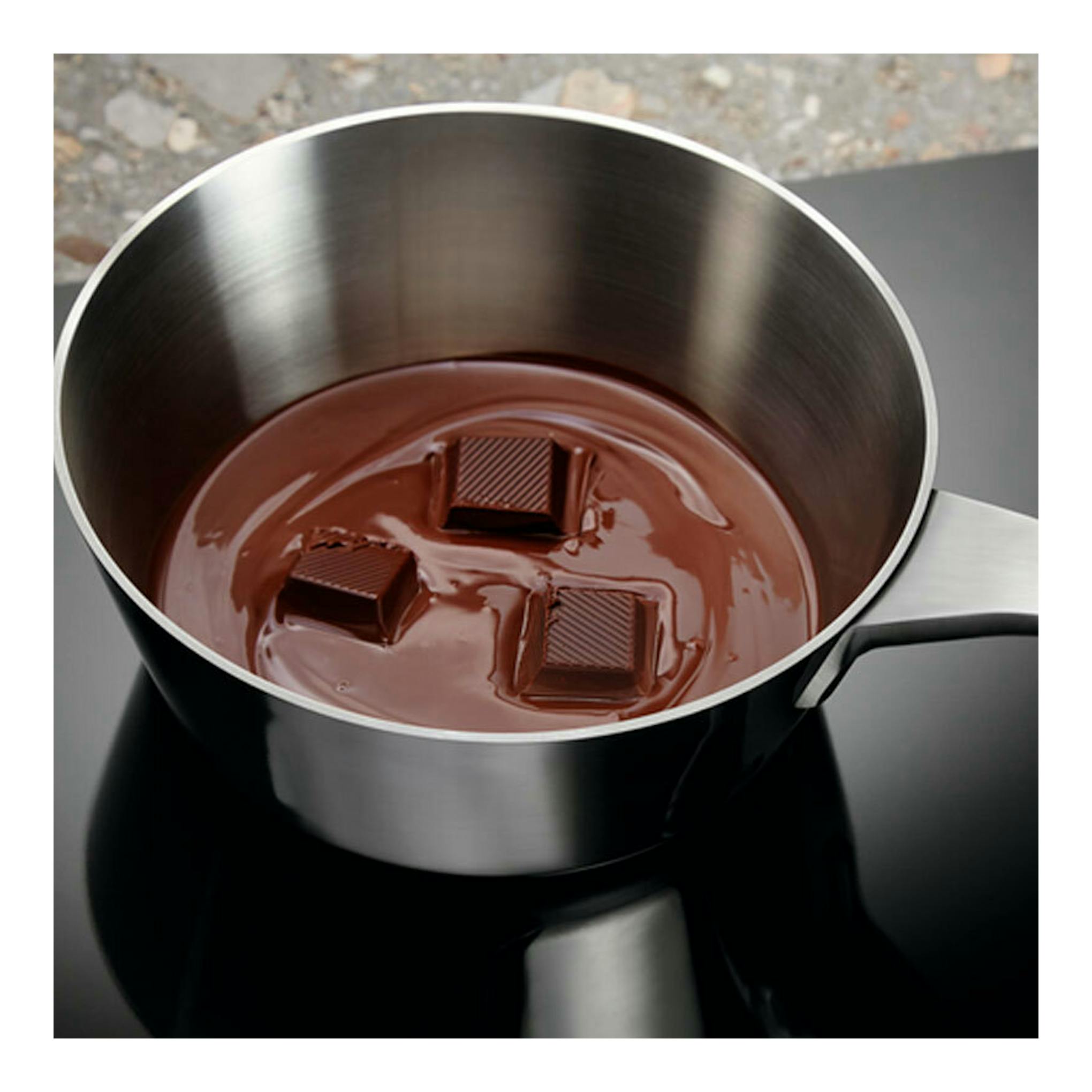 Placa de inducción Electrolux EIV644, cazo de acero con chocolate fundido sobre placa negra.