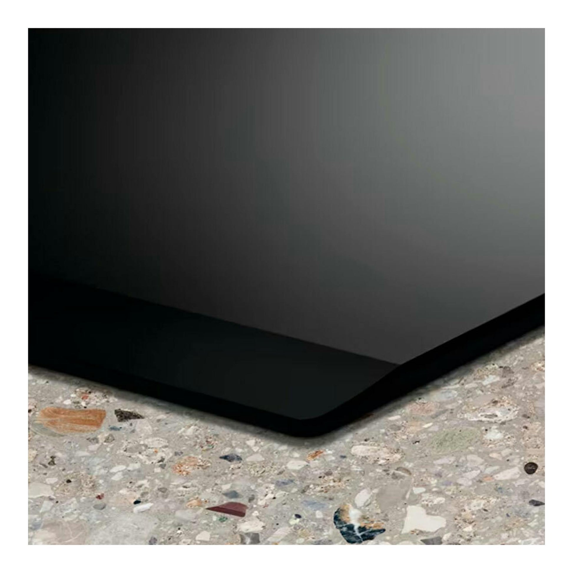 Placa de inducción Electrolux LIT6043 negra, vista en primer plano de una esquina sobre encimera moteada.