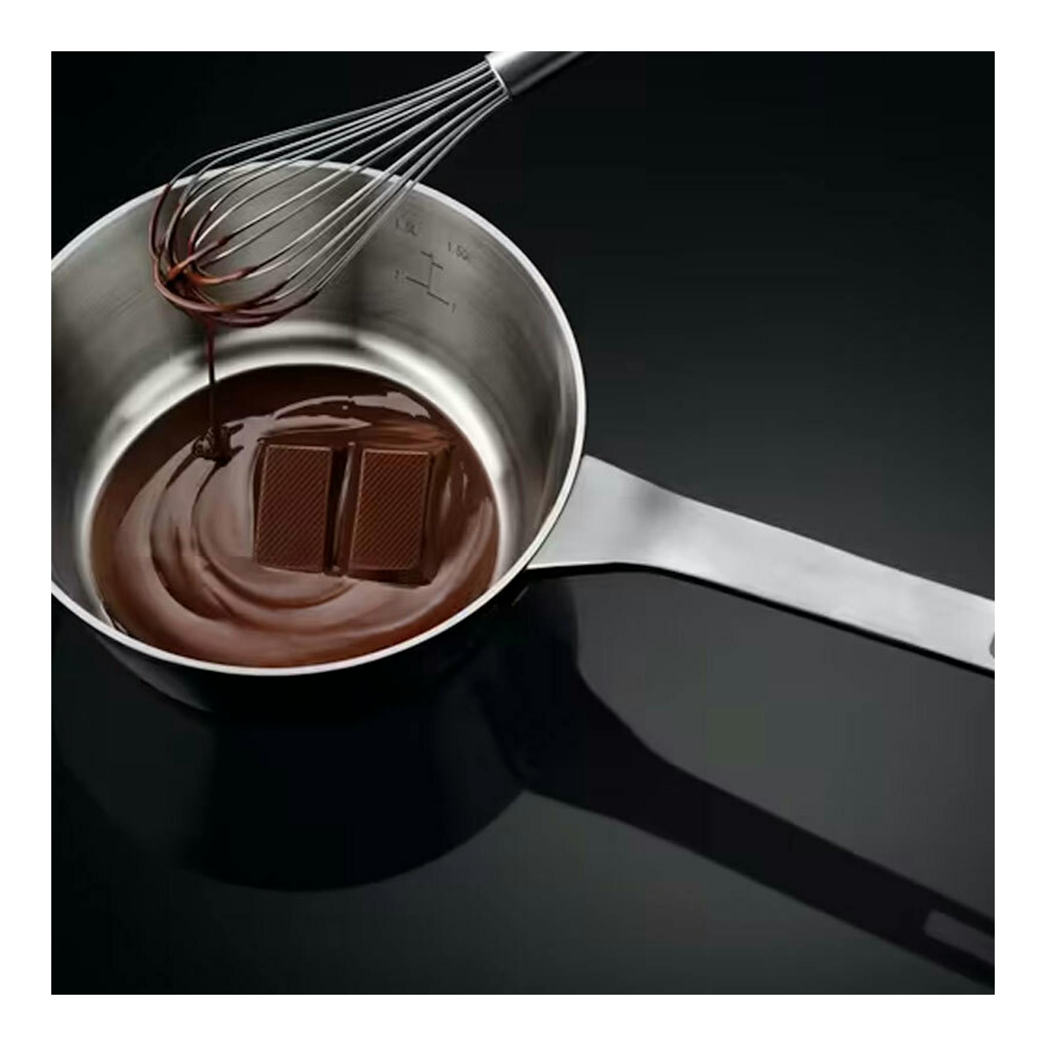 Placa de inducción AEG IKB63302FB negra, con cazo de chocolate y varillas sobre cristal, vista cenital.