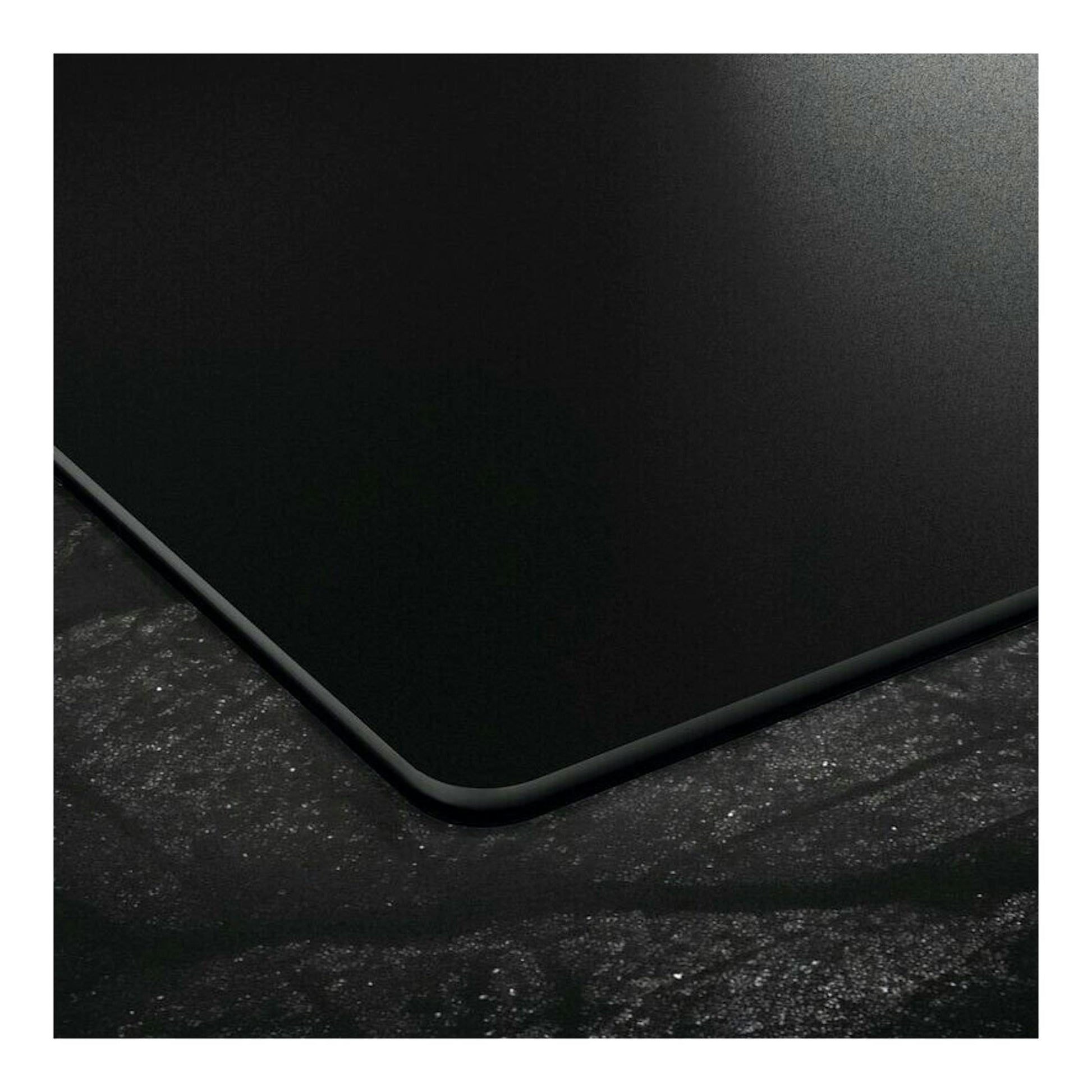 Vista en primer plano de una placa de inducción negra, con esquina redondeada sobre superficie oscura.