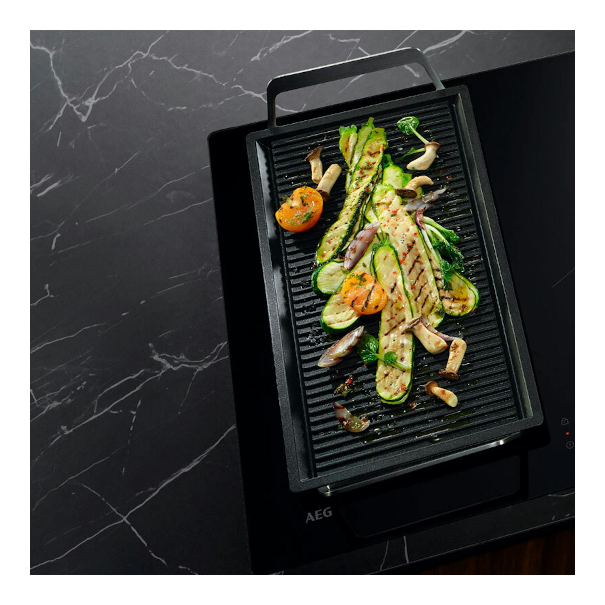 Placa de inducción AEG TO63IQ00IT negra, vista cenital inclinada, con parrilla y verduras.