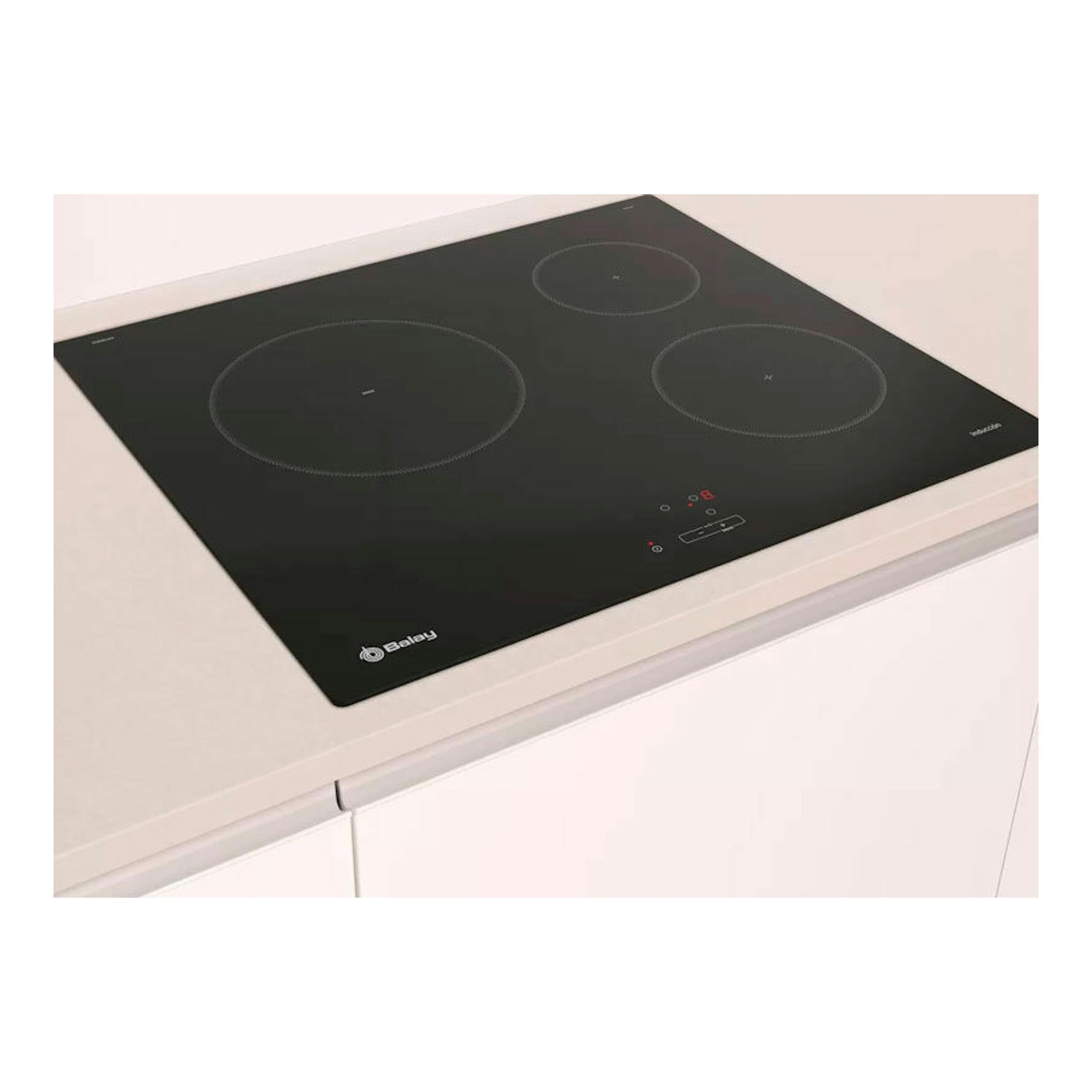Placa de inducción Balay 3EB864EN negra, vista en ángulo sobre encimera blanca, con tres zonas de cocción.
