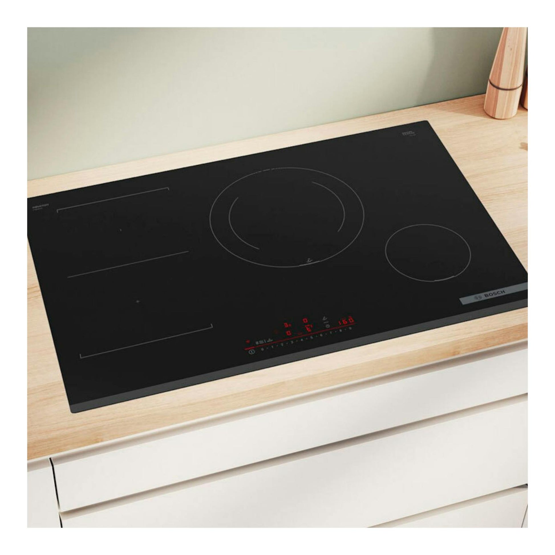 Placa de inducción Bosch PVS831HC1E negra, vista en ángulo sobre encimera de madera, con mandos táctiles rojos.
