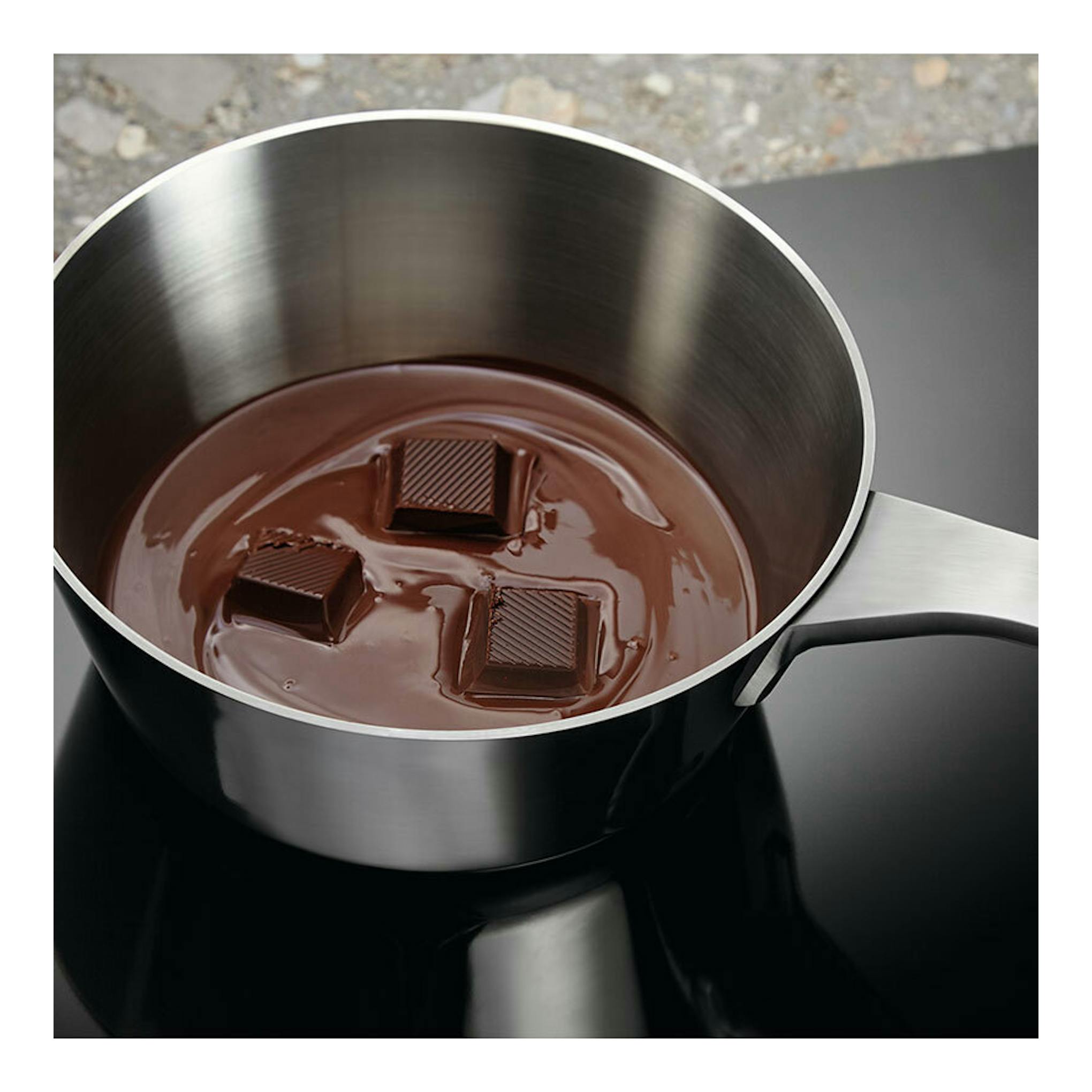 Placa de inducción Electrolux CIB60320CK, vista cenital, con cazo de acero inoxidable y chocolate fundido.