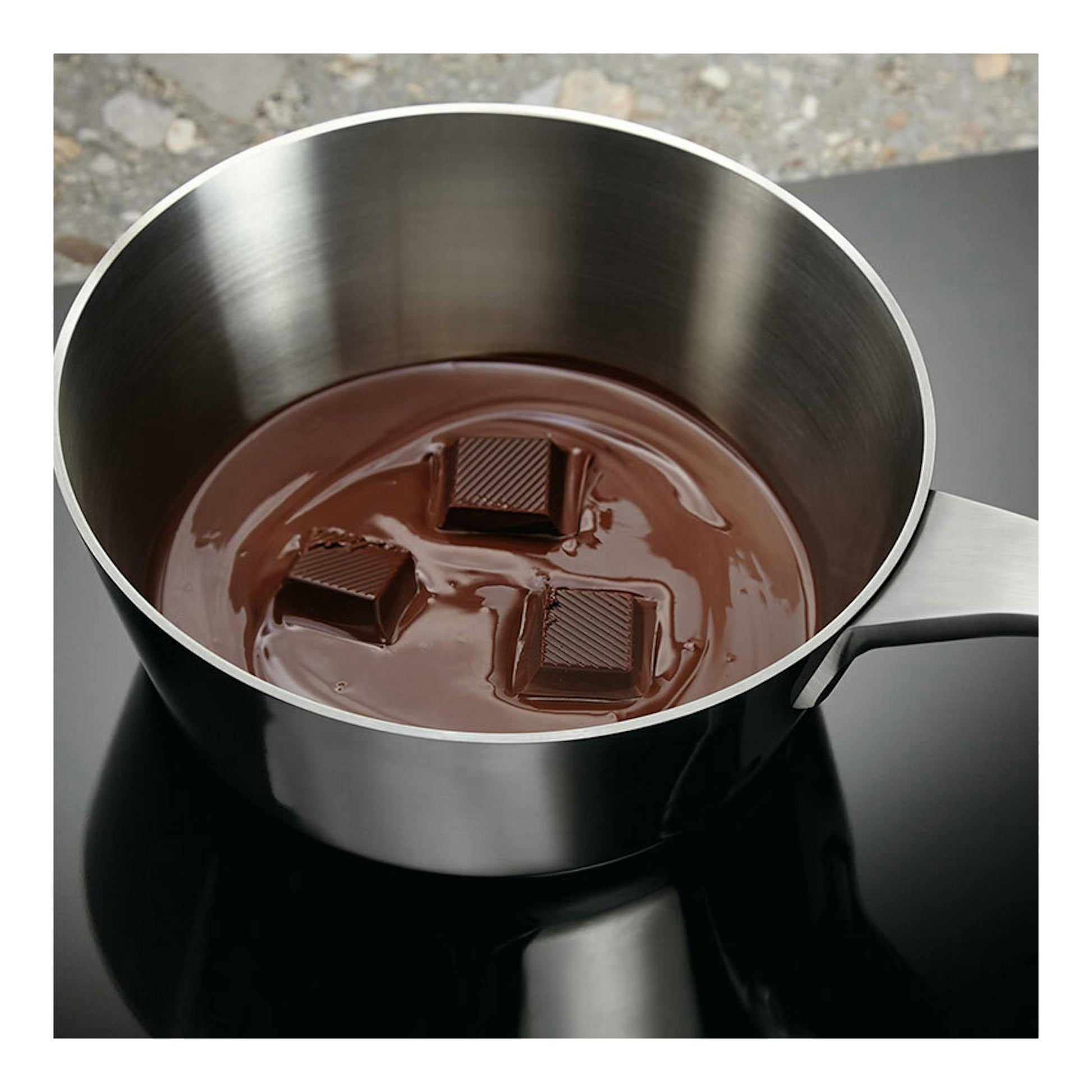 Placa de inducción Electrolux EIV633 negra, vista cenital parcial, con cazo de acero y chocolate fundido.
