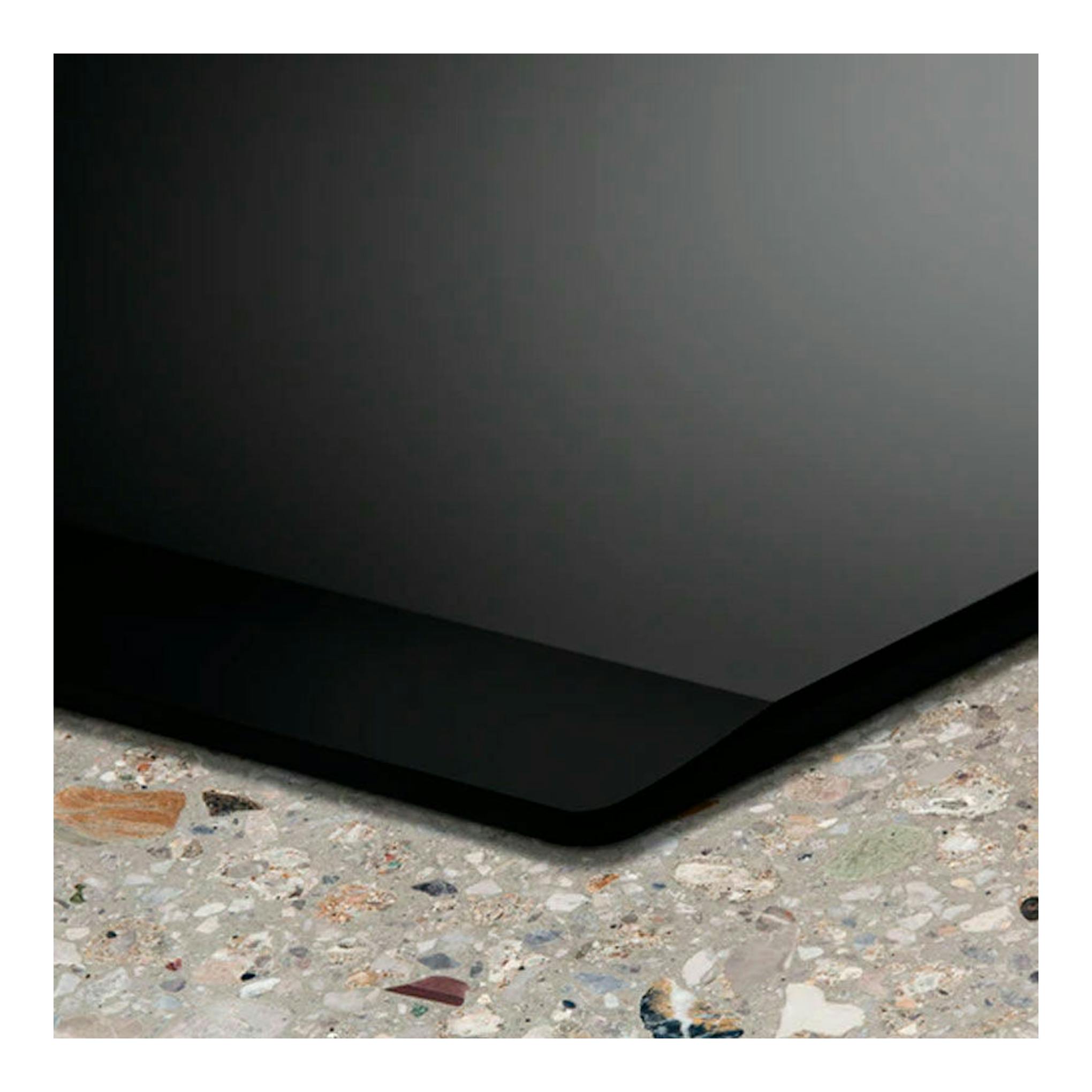 Placa de inducción Electrolux LIL60336, vista en primer plano de una esquina negra sobre encimera moteada.
