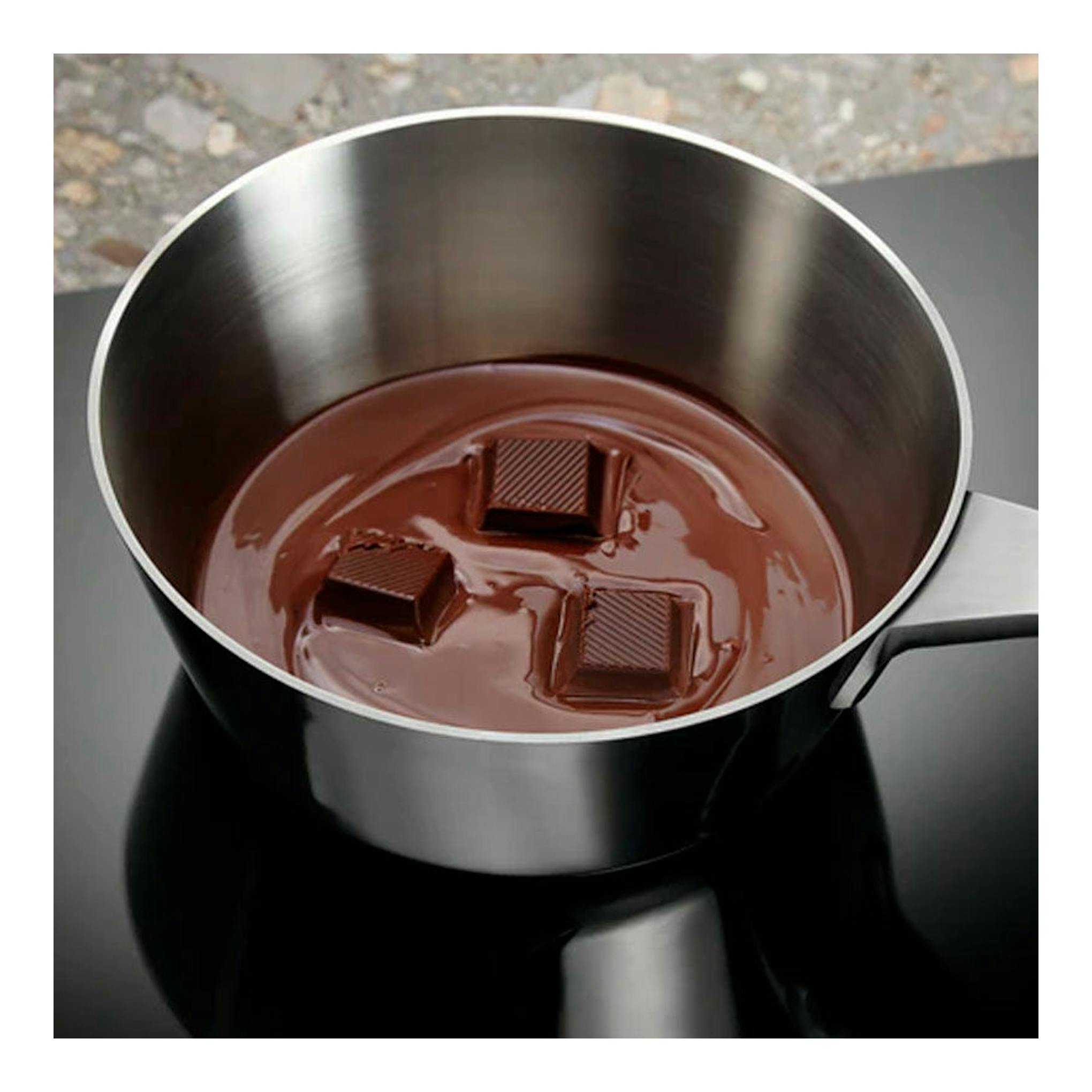 Placa de inducción Electrolux LIL60336 negra, vista cenital, con cazo de acero y chocolate fundido.