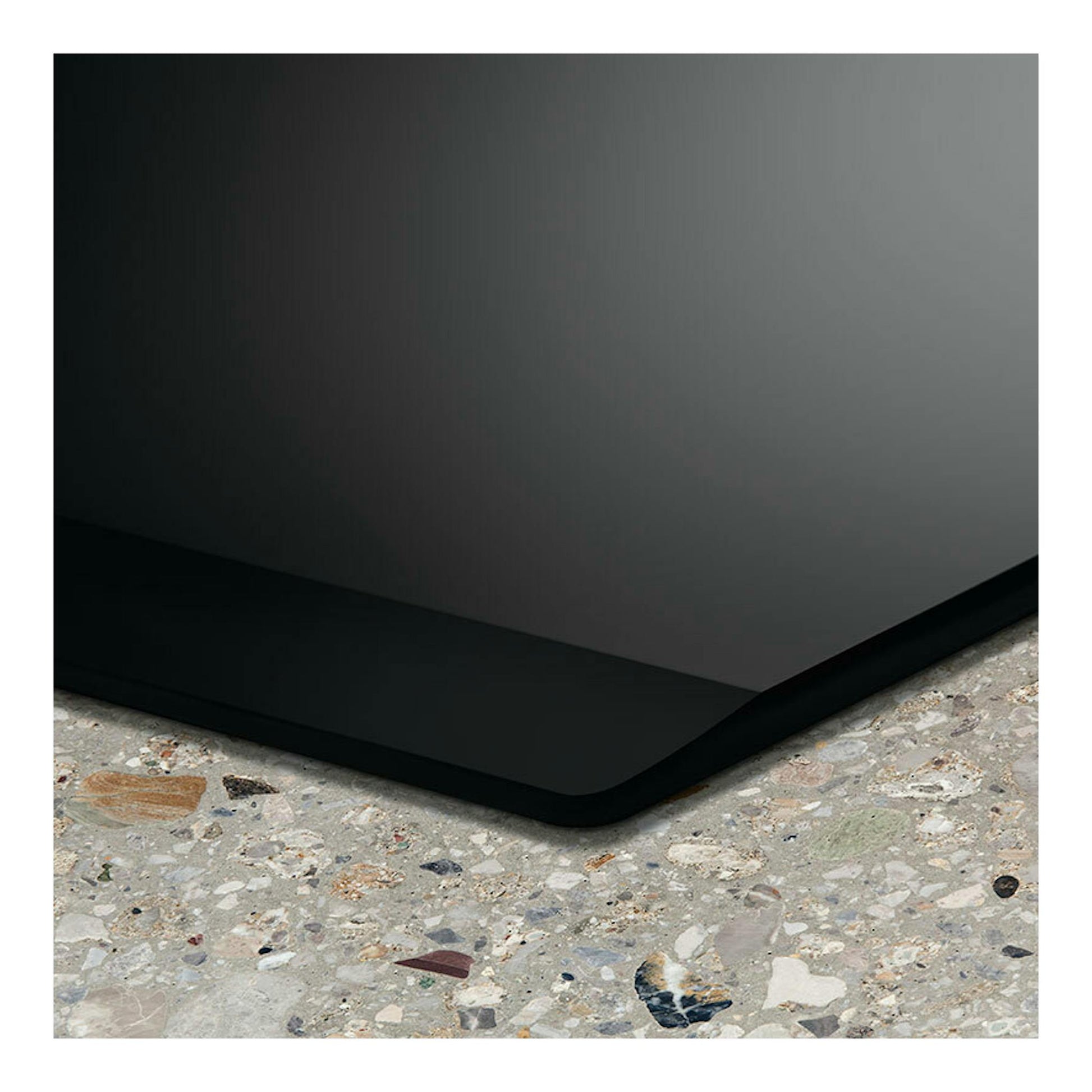 Placa de inducción Electrolux LIS62341 negra, vista en primer plano de una esquina sobre encimera moteada.