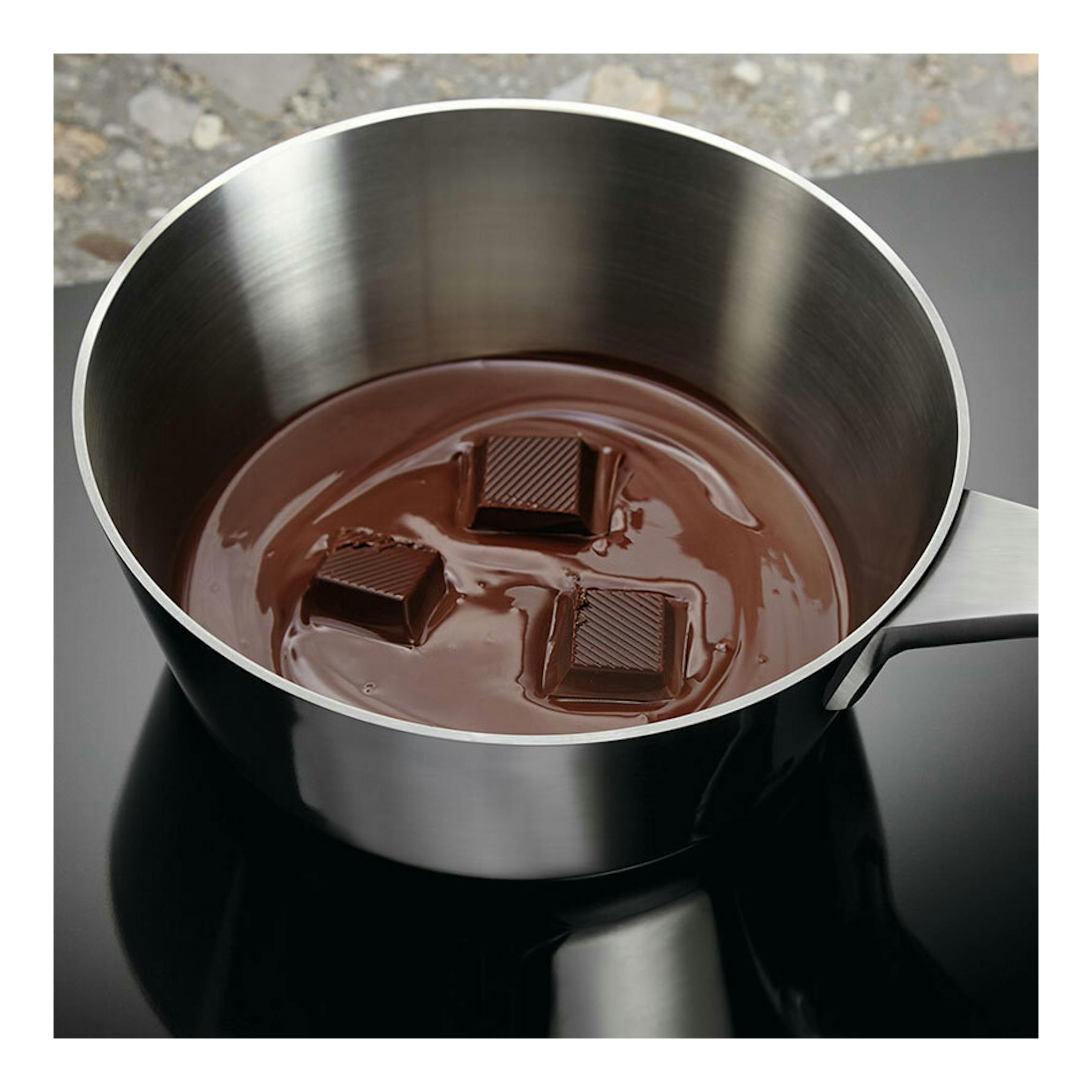 Placa de inducción Electrolux LIS62341 negra, con cazo metálico y chocolate fundido, vista cenital.