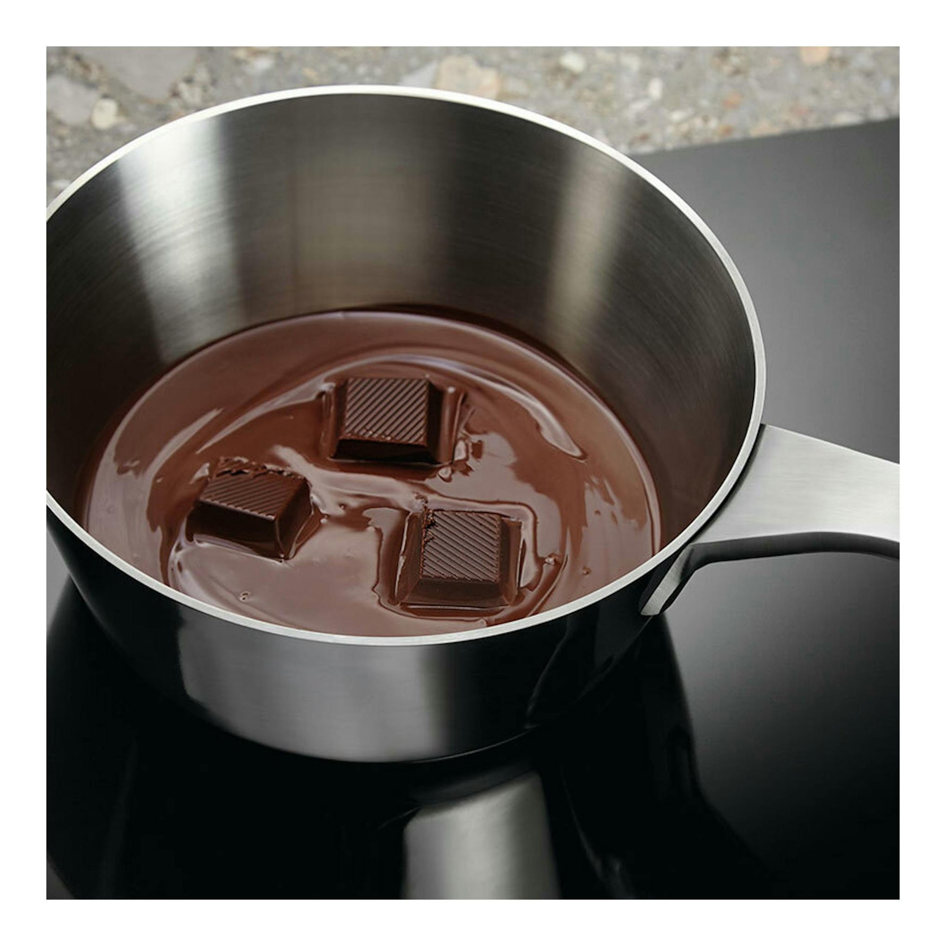 Placa de inducción Electrolux LIV63340CK negra con cazo de acero y chocolate fundido, vista cenital.