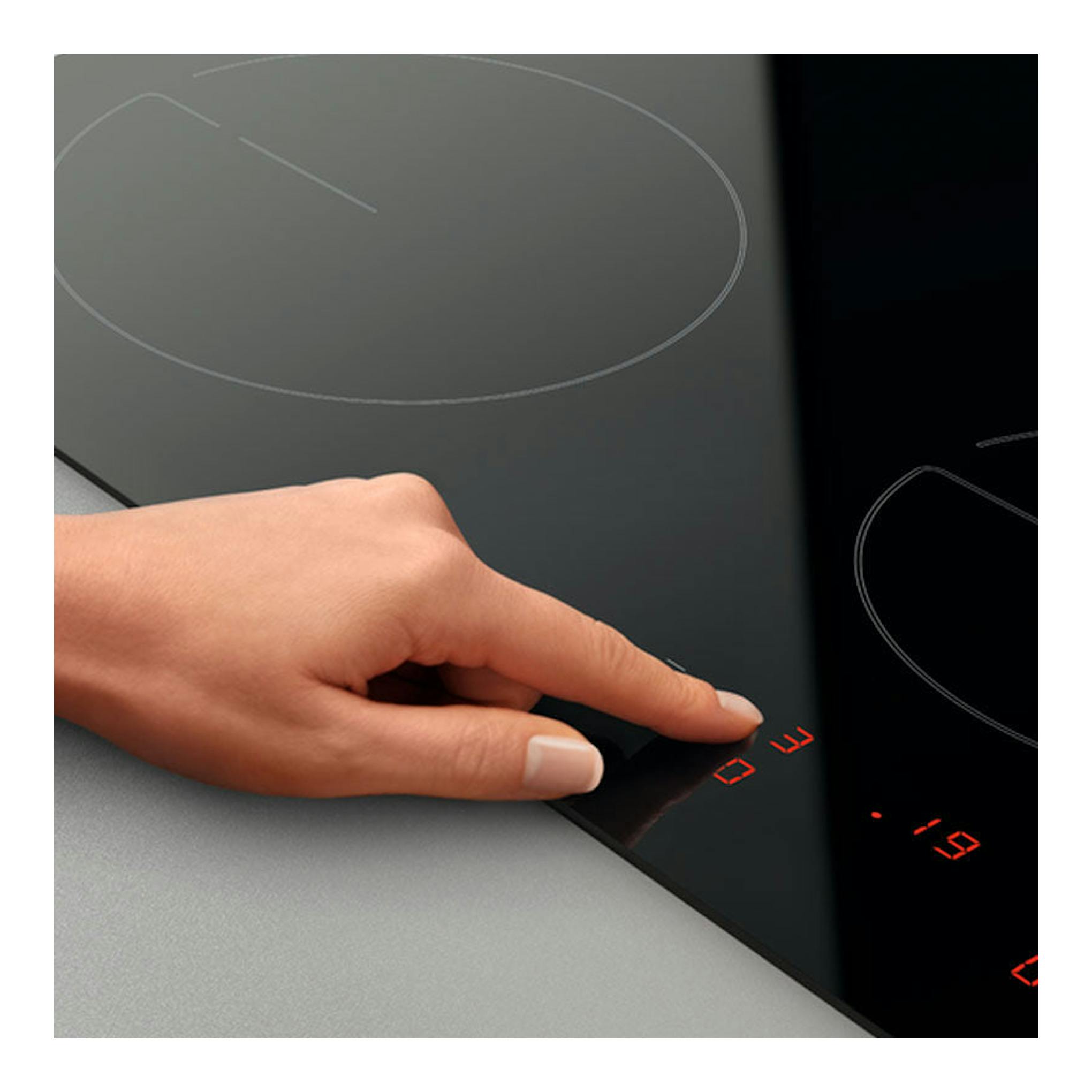 Placa vitrocerámica Zanussi ZHRN639K negra, vista en ángulo, con mano tocando los controles táctiles rojos.