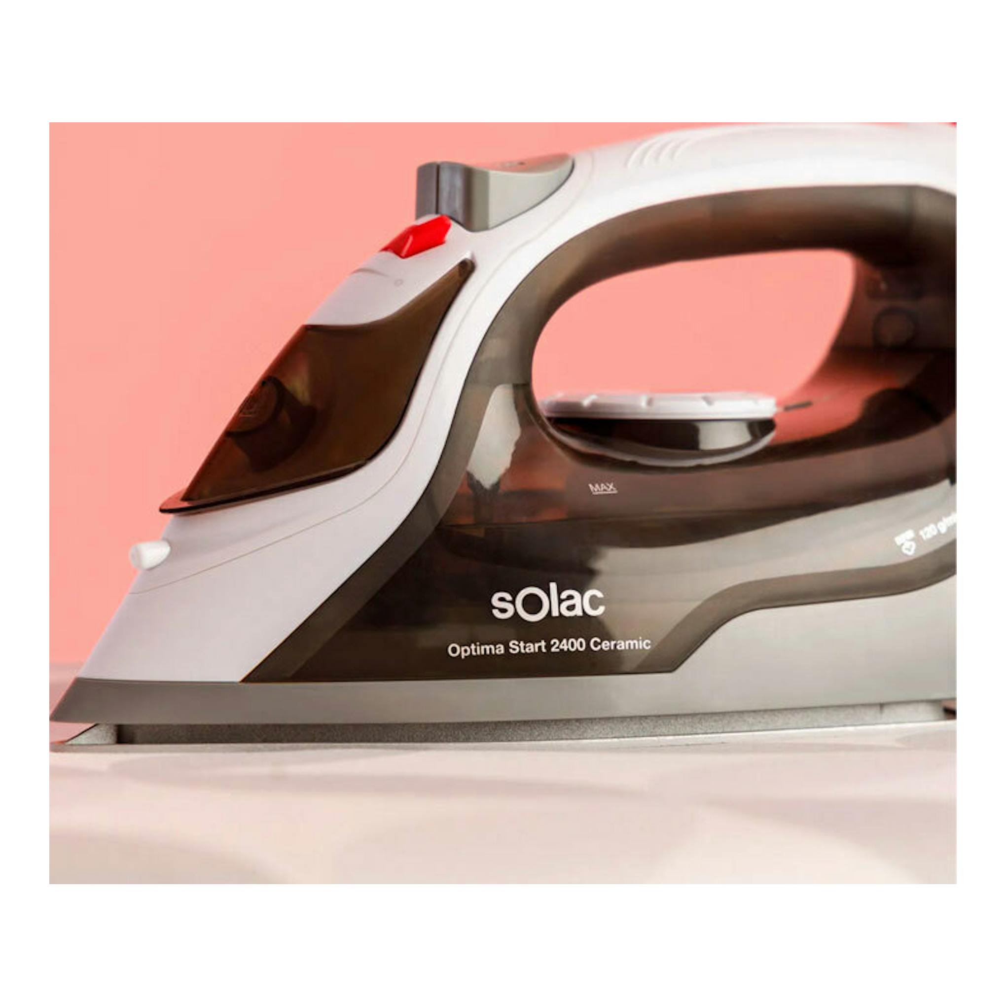 Plancha de vapor Solac Optima Start 2400 Ceramic, vista lateral, blanca y negra, sobre fondo rosa.