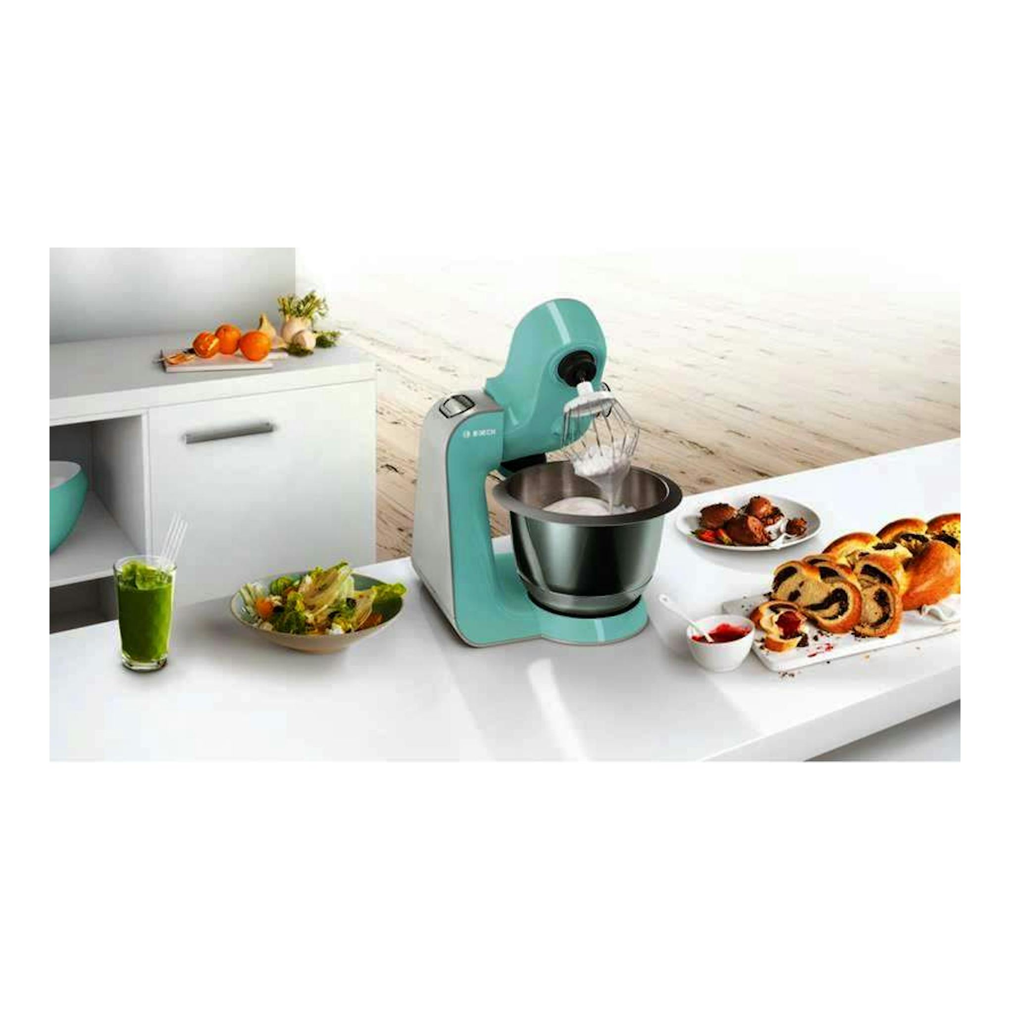 Robot de repostería Bosch MUM58020 turquesa y plateado, vista frontal tres cuartos, con bol y varillas.