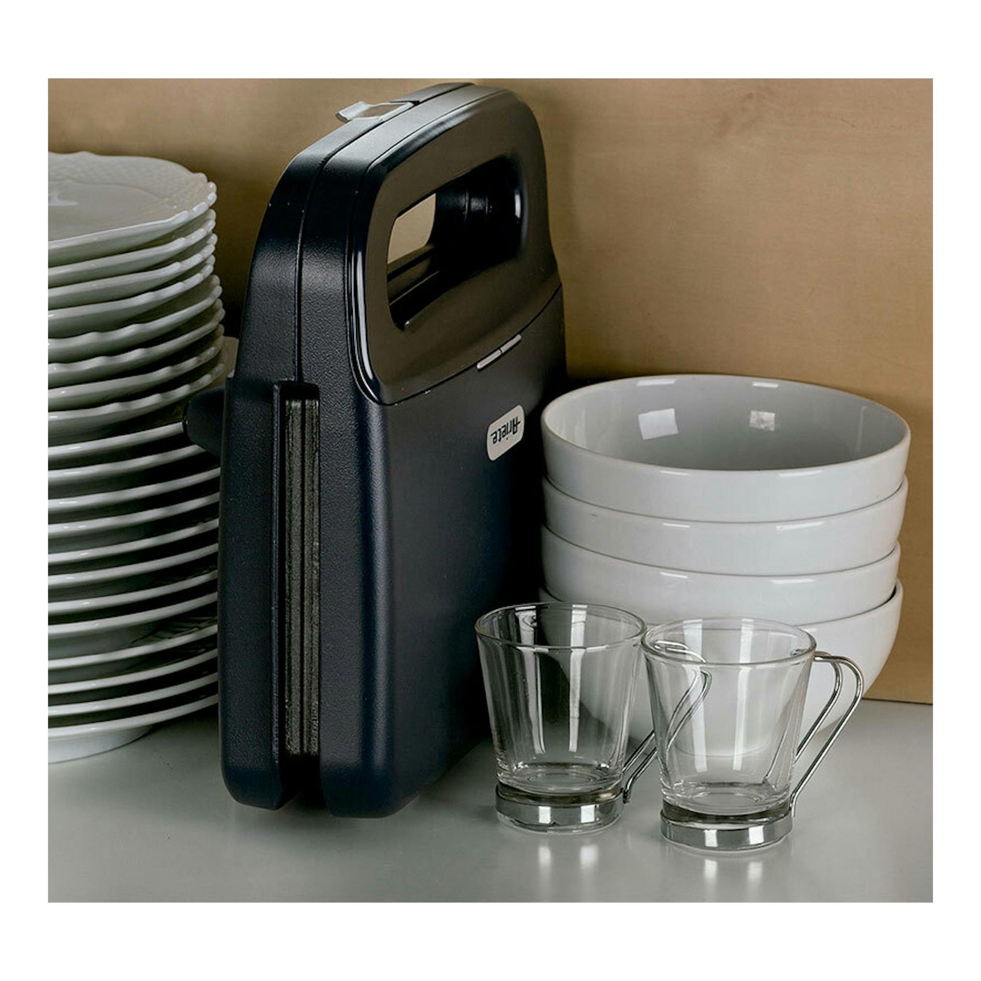 Sandwichera Ariete Breakfast grafito, vista frontal lateral, de pie junto a platos y tazas.
