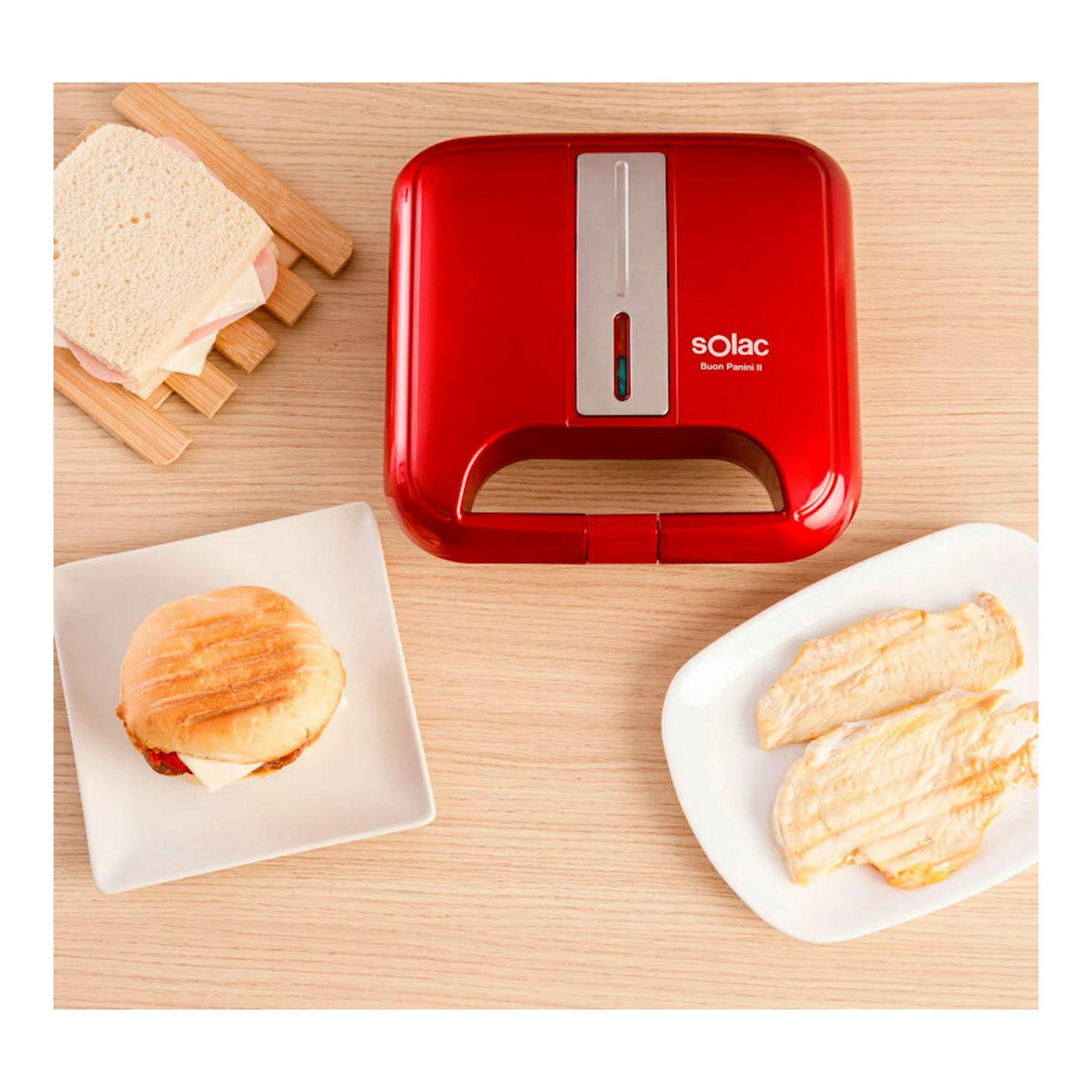 Sandwichera Solac SD5058 roja, vista superior sobre mesa de madera, con sándwiches servidos alrededor.