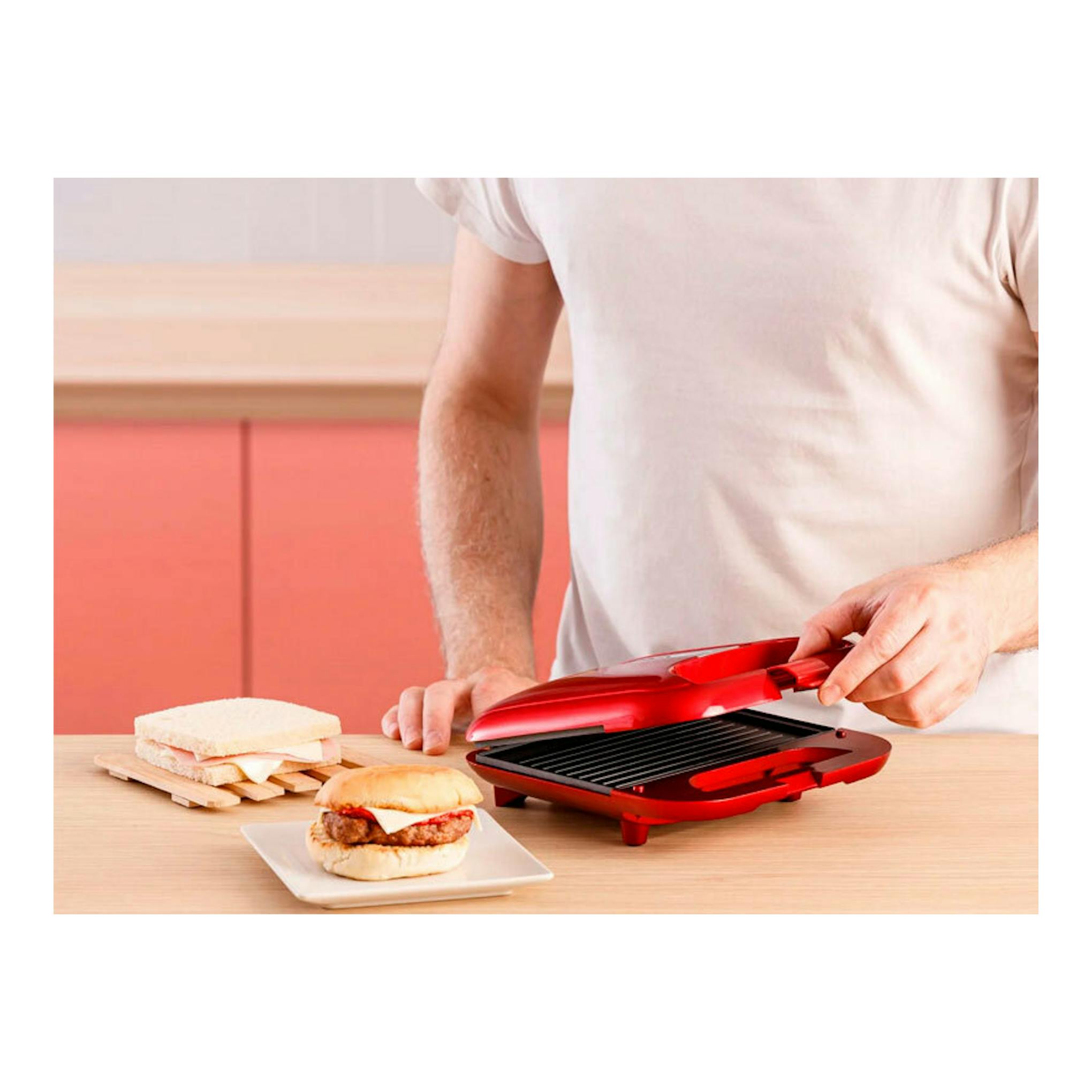 Sandwichera Solac SD5058 roja, abierta sobre una mesa, con una persona levantando la tapa.