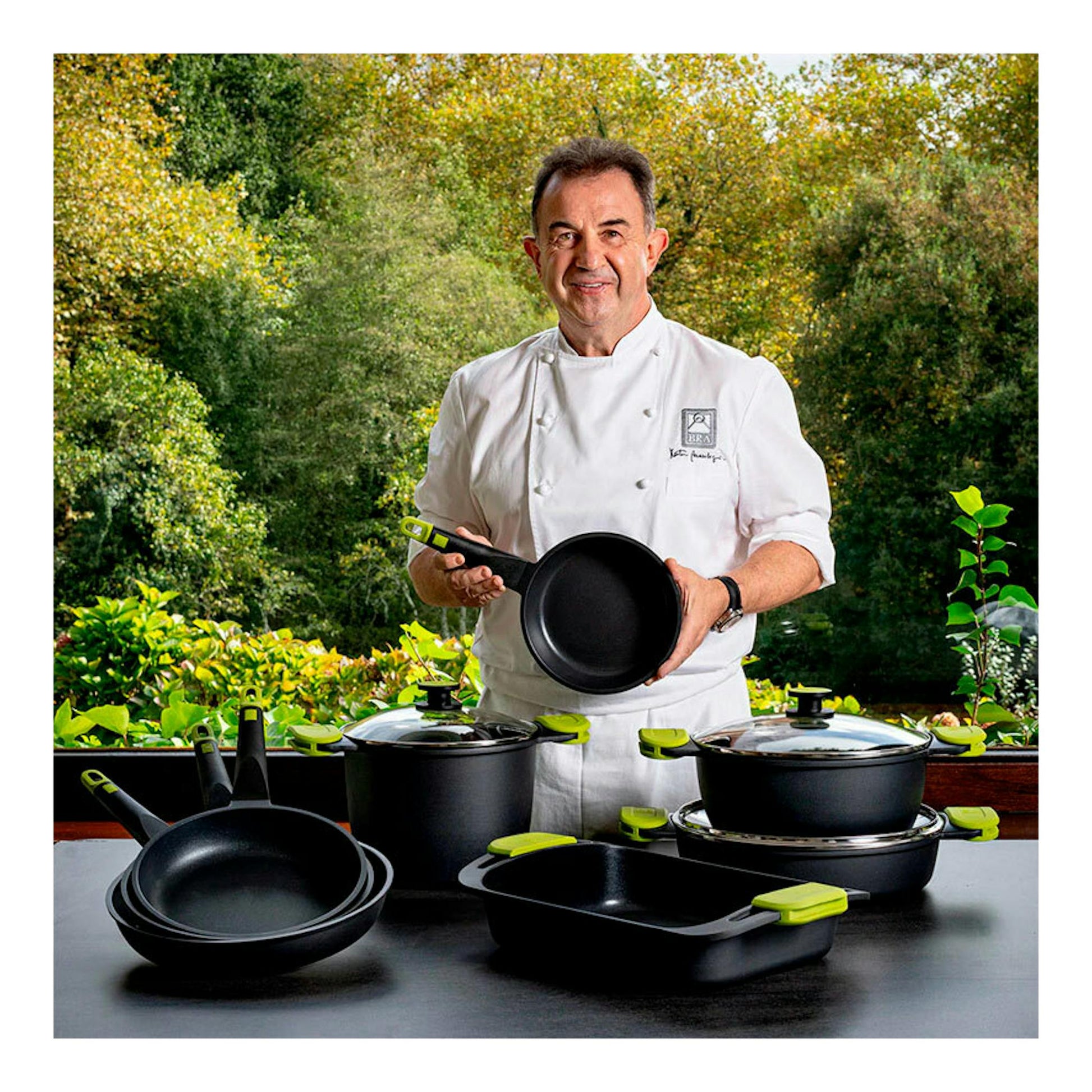 Sartén Bra Foodie 20 negra con mango verde, sostenida por un chef, con otras piezas del set.