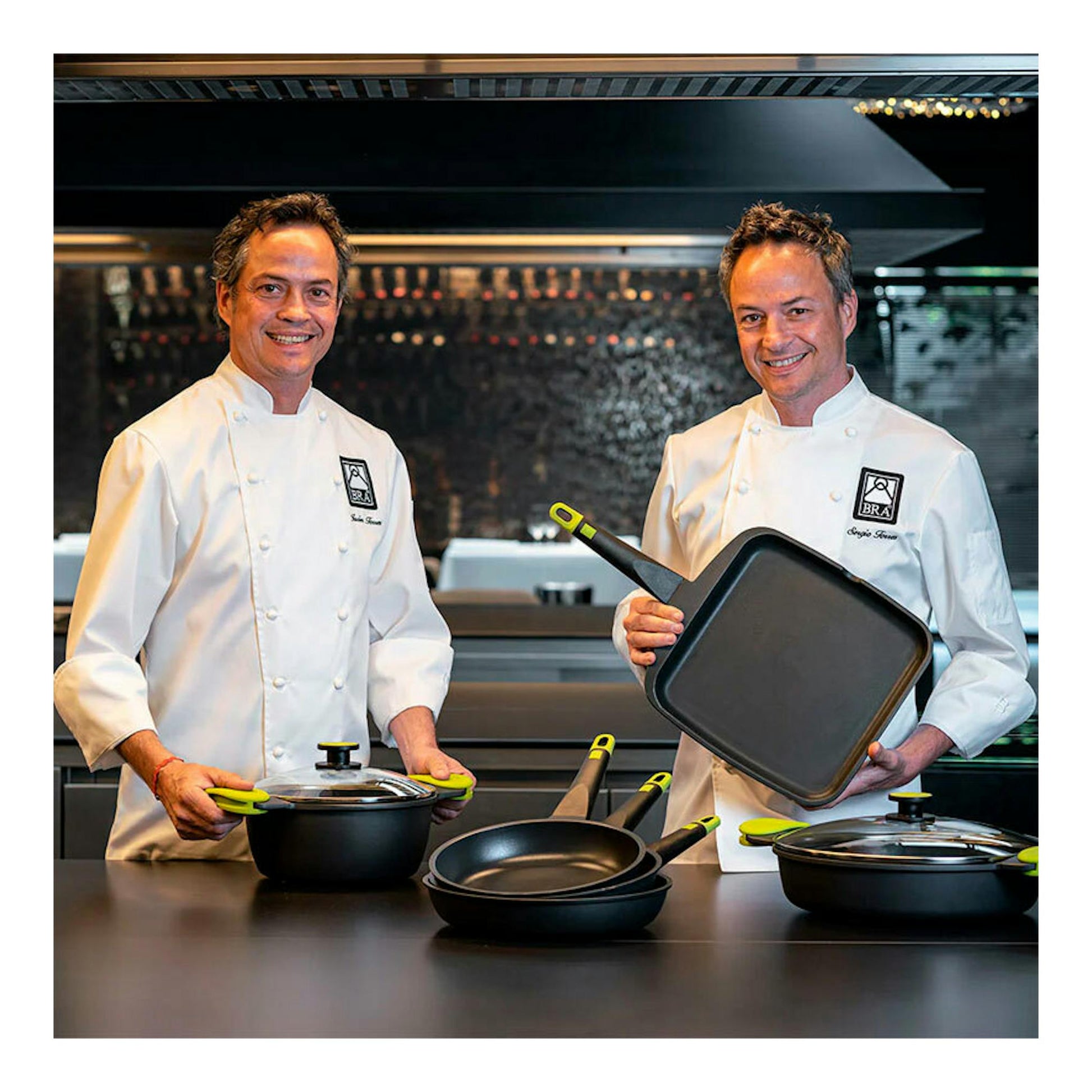 Dos chefs con sartén Bra Foodie 28 negra y otras piezas de cocina sobre una mesa.