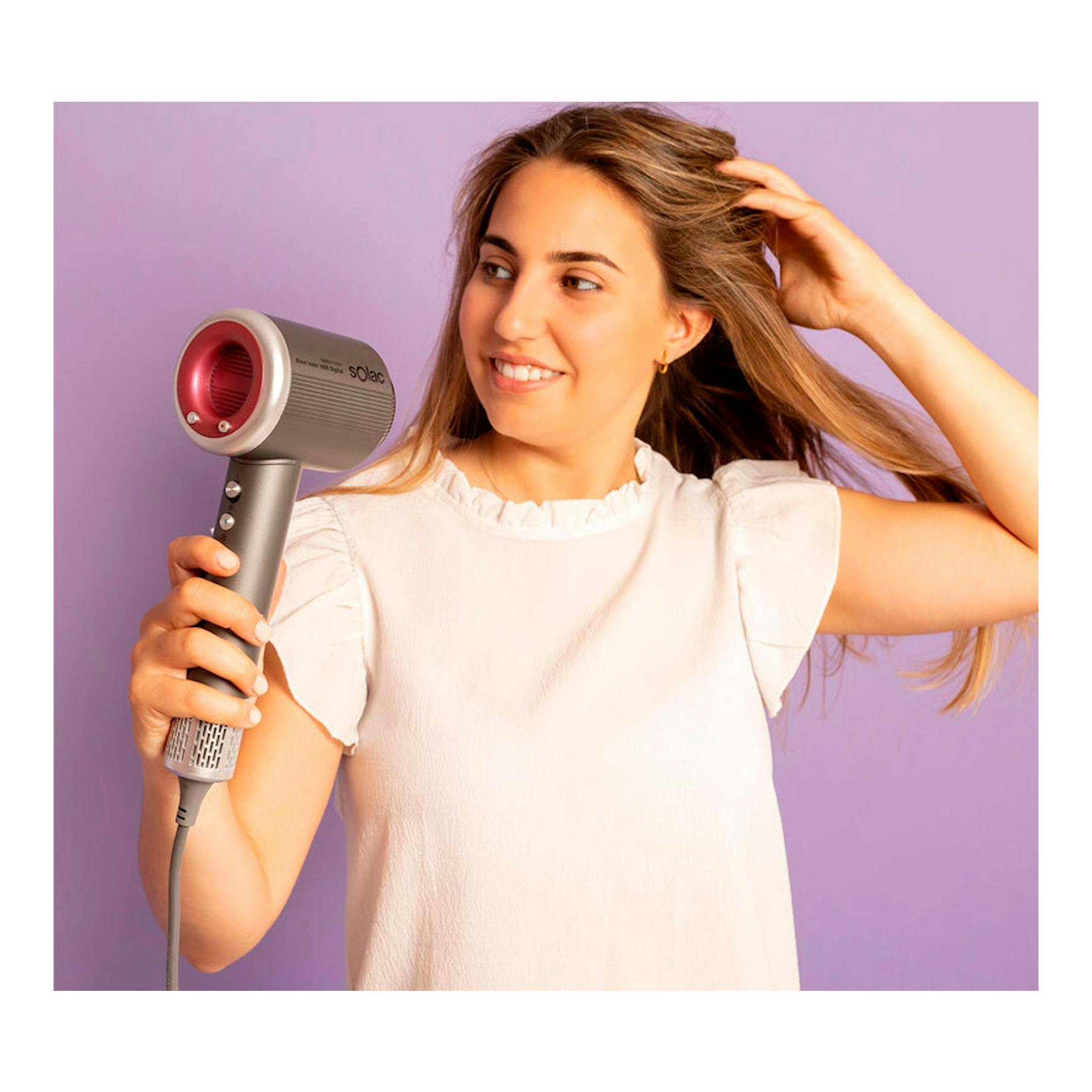 Secador Solac SB7950 Blast Ionic 1600 Digital gris y rosa, en mano junto a una mujer peinándose.