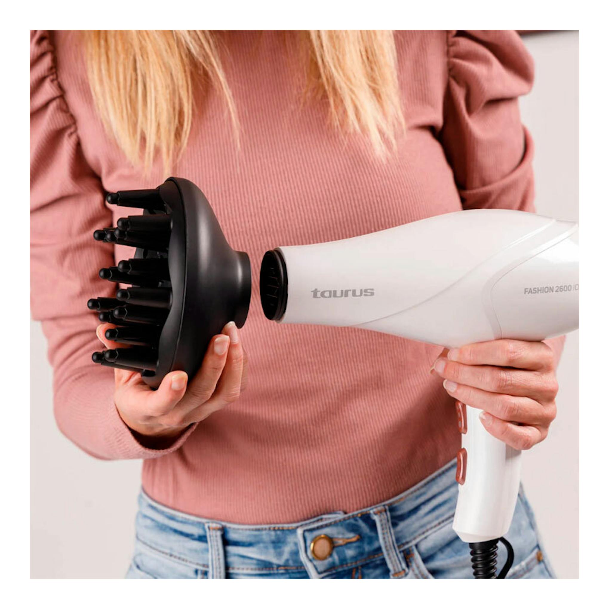 Secador Taurus Fashion 2600 Ionic blanco con difusor negro, sostenido por una persona en vista frontal.