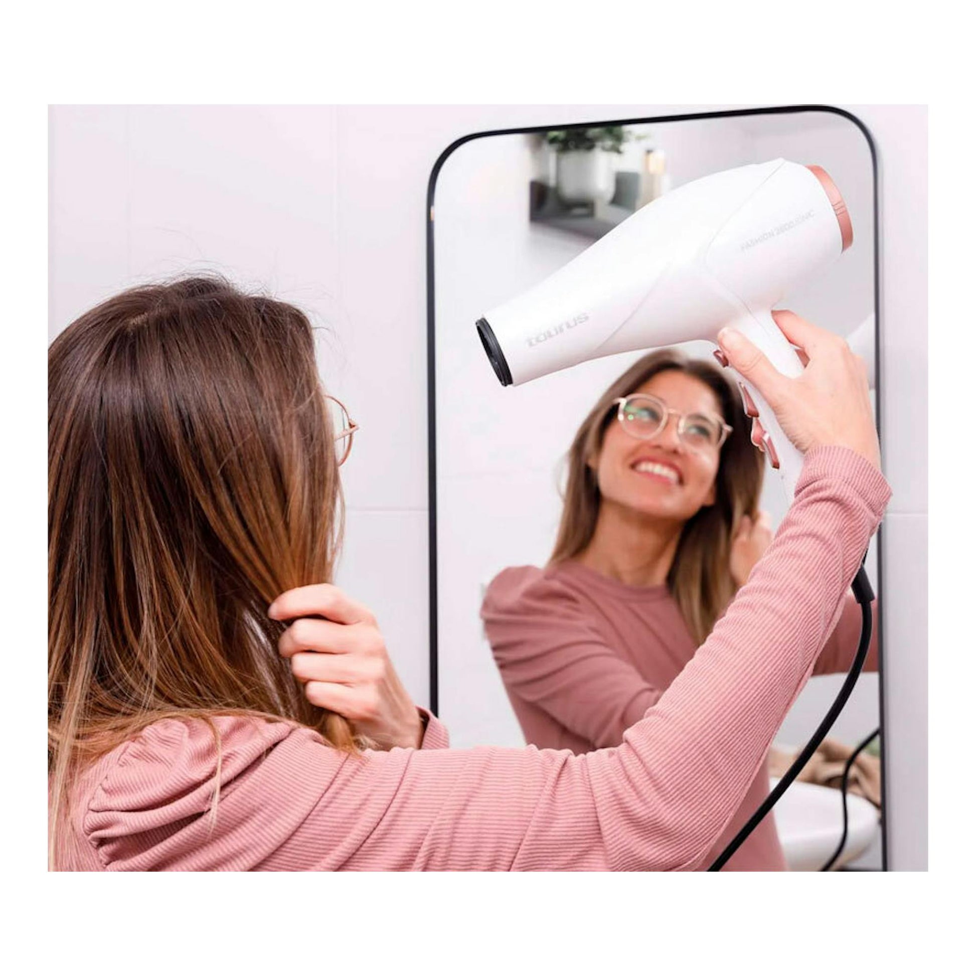 Secador Taurus Fashion 2600 Ionic blanco, visto de perfil, usado frente a un espejo por una mujer.