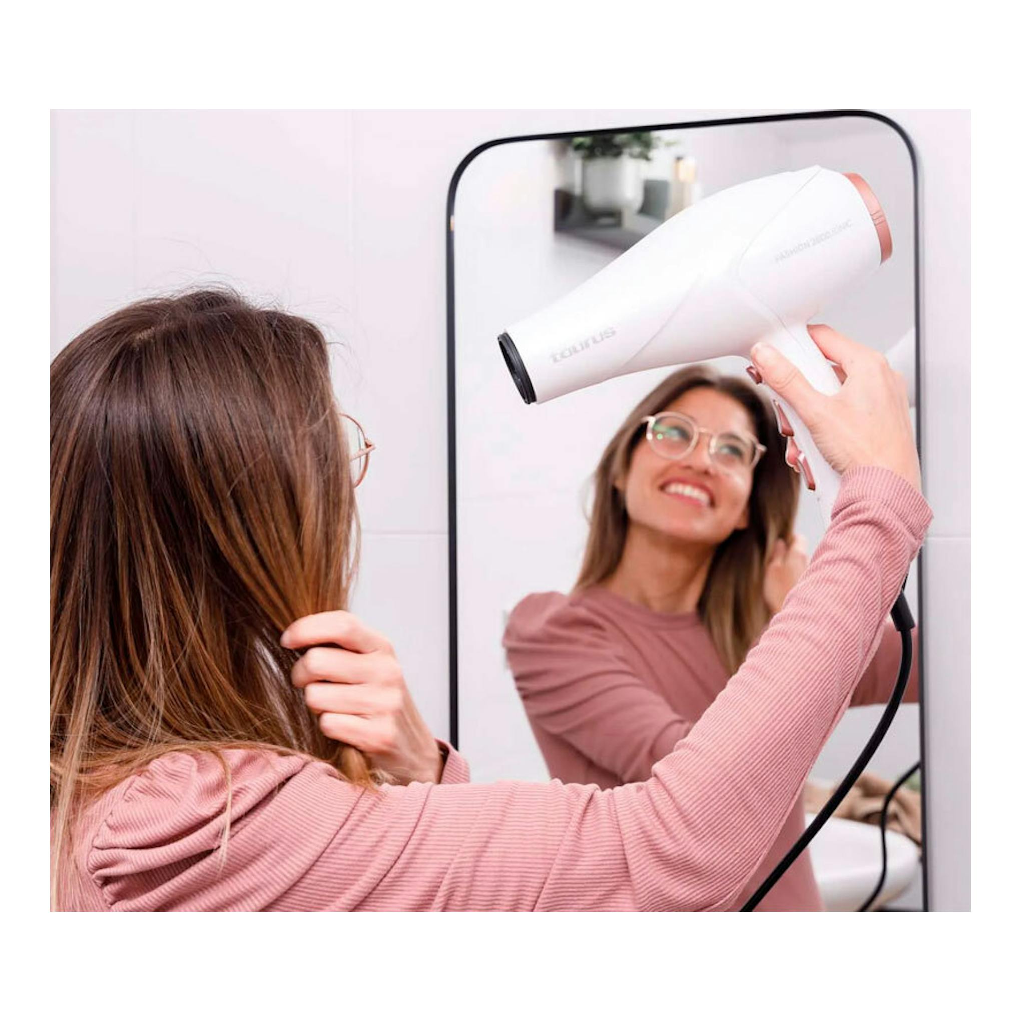 Secador Taurus Fashion 2600 Ionic blanco, visto de perfil, usado frente a un espejo por una mujer.